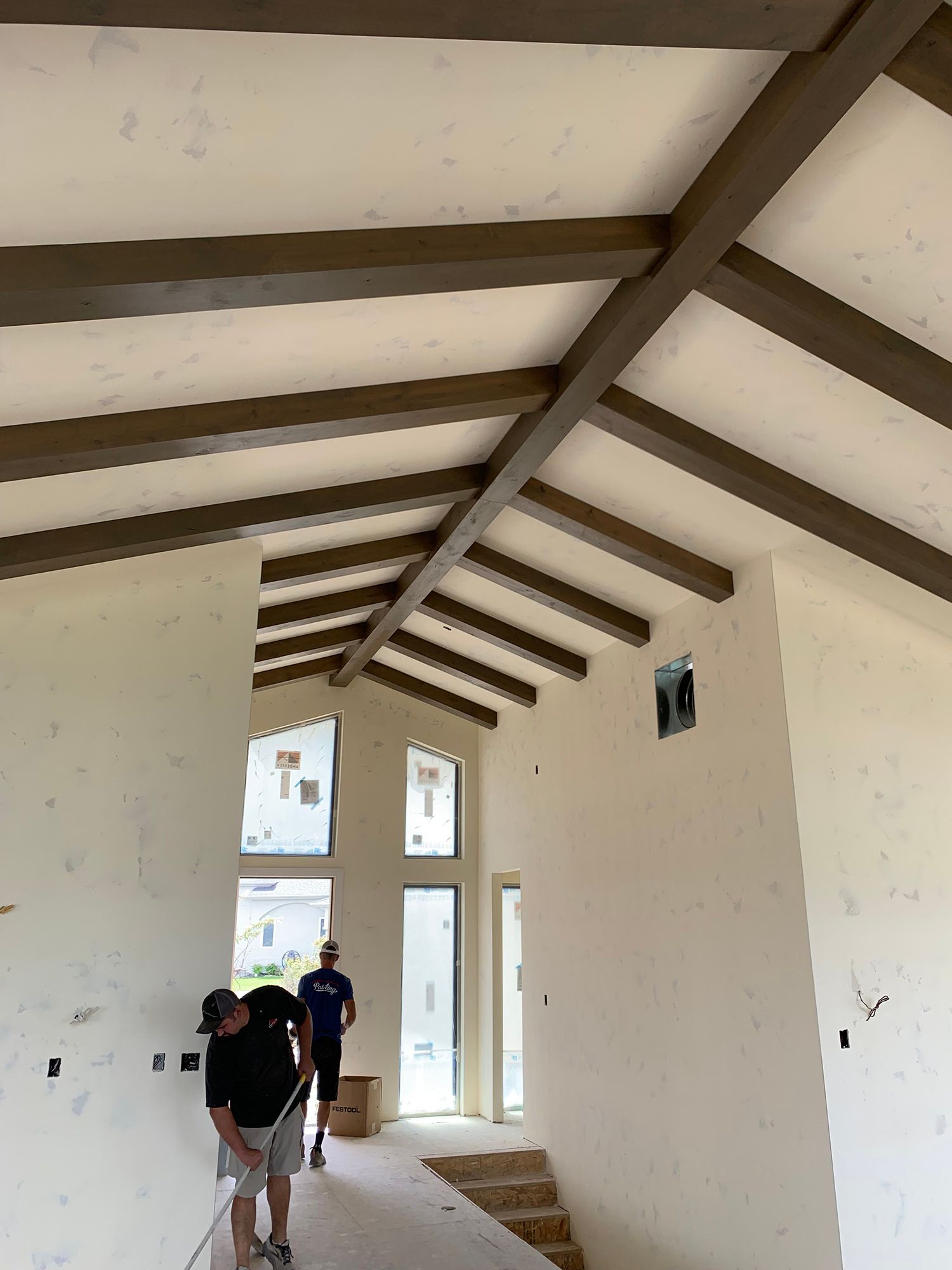 Long hallway under construction with exposed beams and two workers carrying materials.