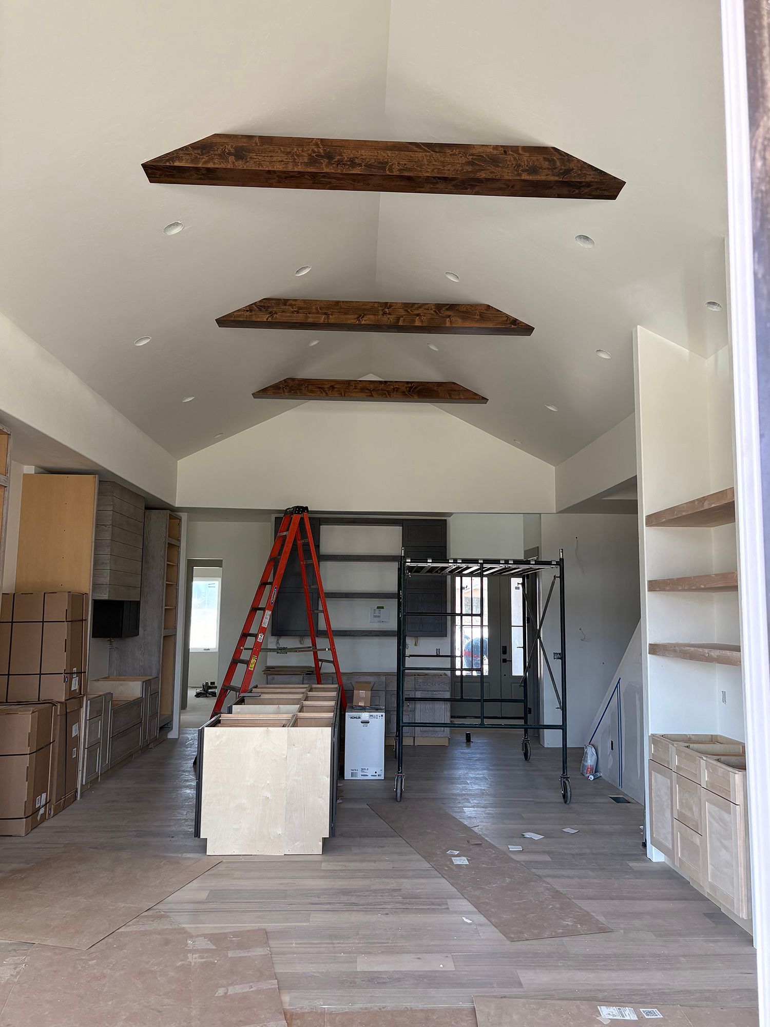 Interior under renovation with ladder, scaffold, boxes, and exposed ceiling beams