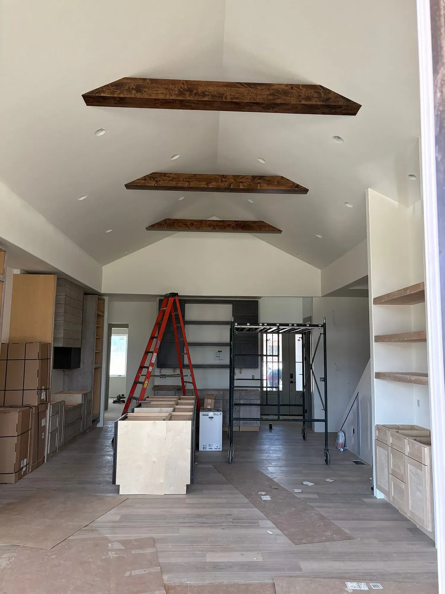 Empty room under renovation with exposed wood beams, a ladder, and construction materials stacked inside.