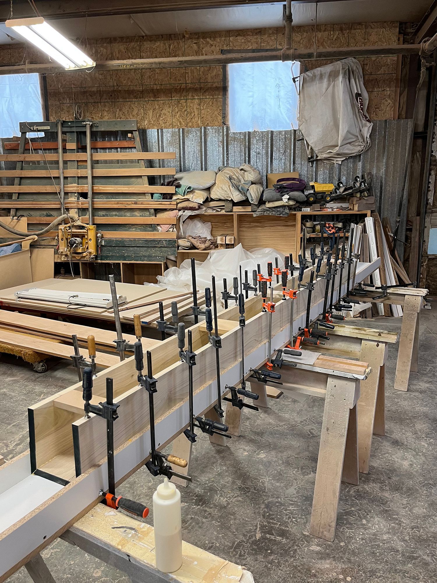 Woodworking shop with long boards clamped on benches and shelves of tools in the background