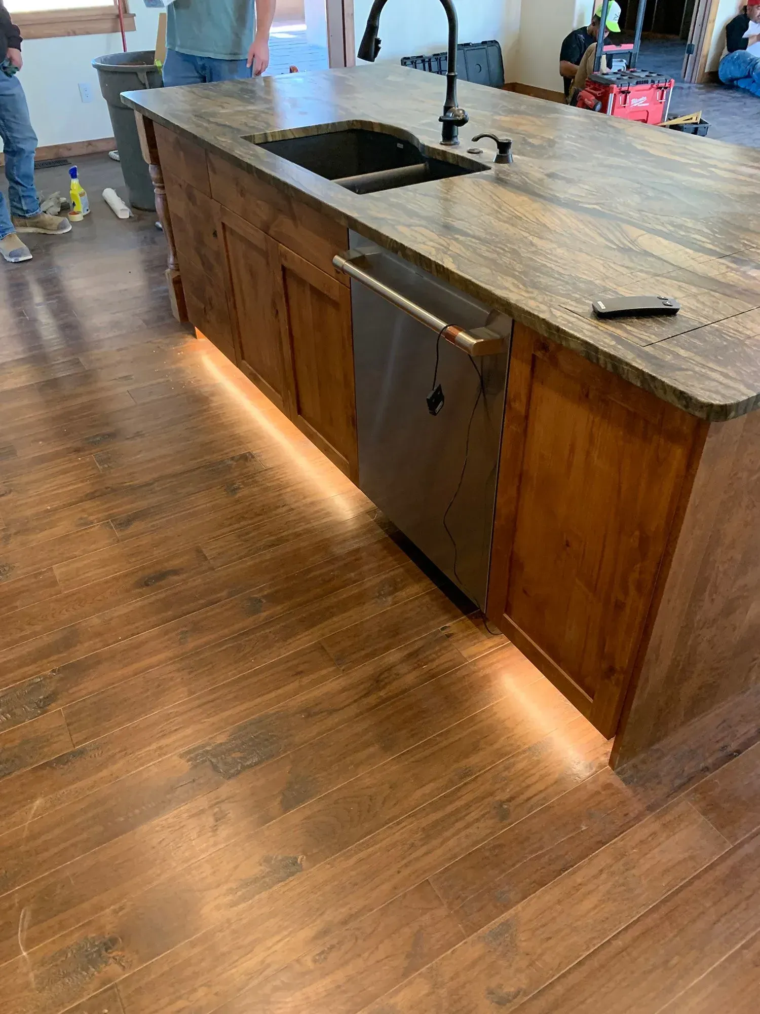 Kitchen island with stone countertop, sink, and under-cabinet lighting on a hardwood floor.