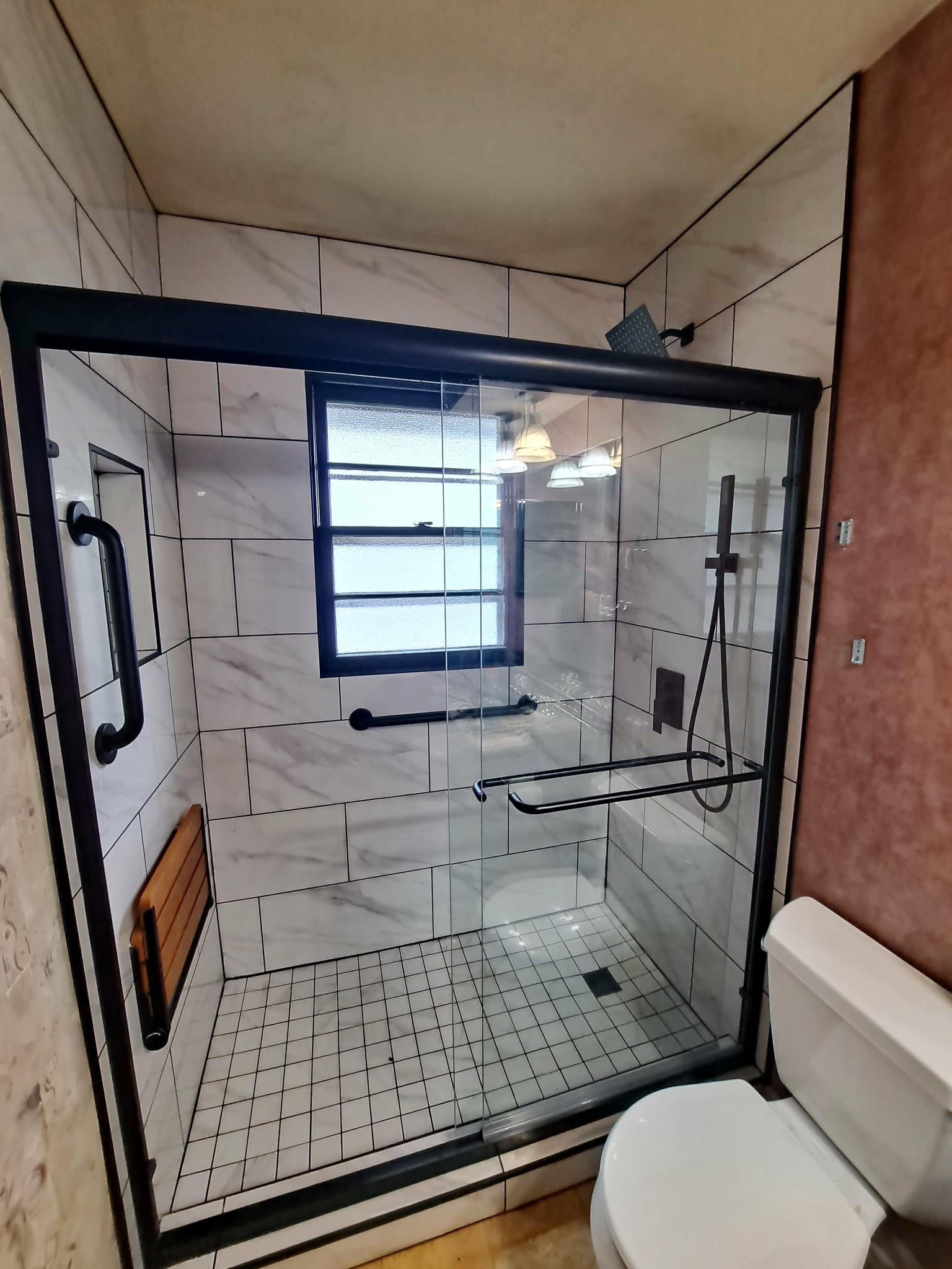 Modern bathroom with a glass shower enclosure, grab bar, and folding seat.