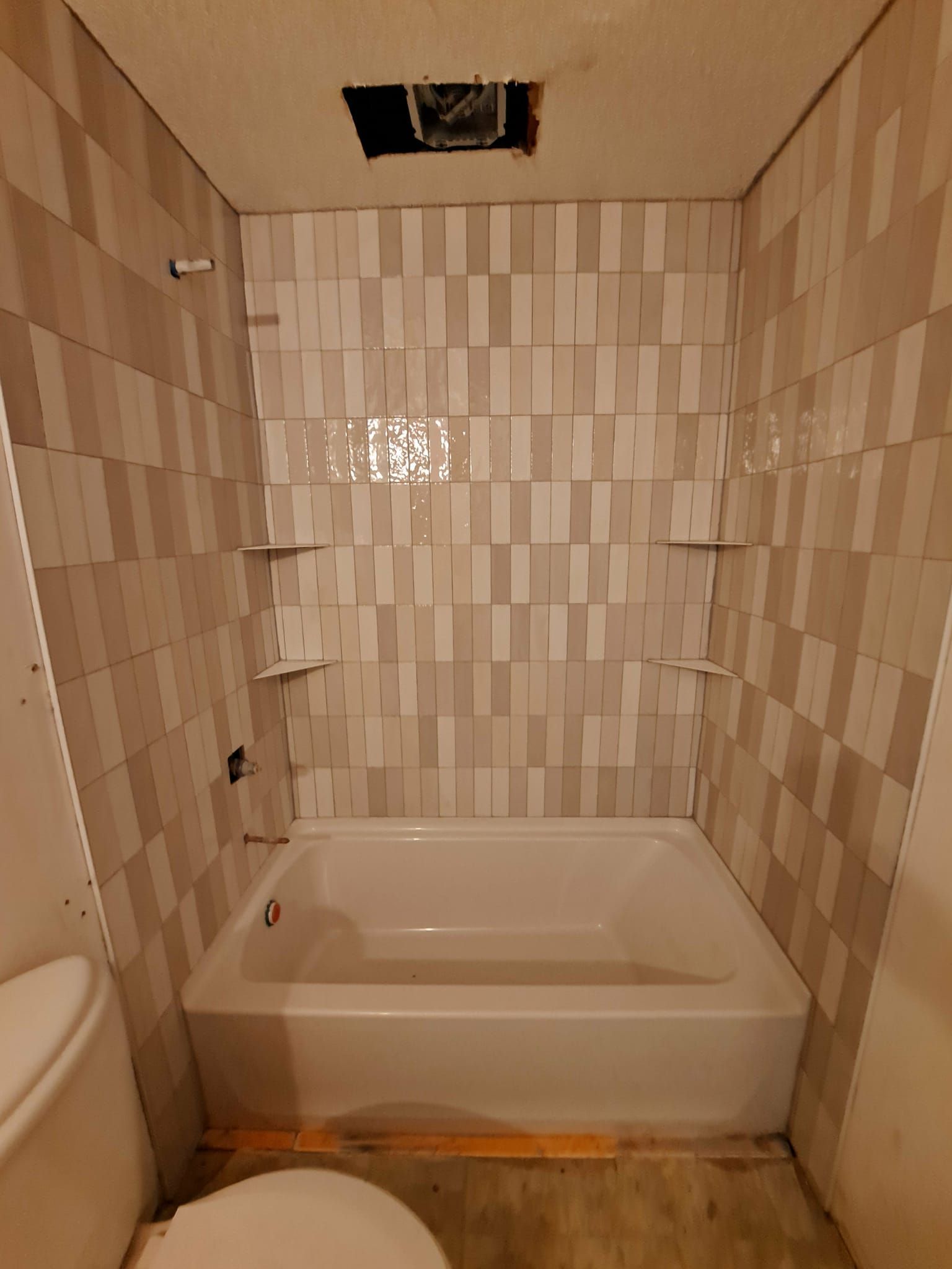 Bathroom remodel: white tub, tiled walls in cream and gray, and three built-in shelves.