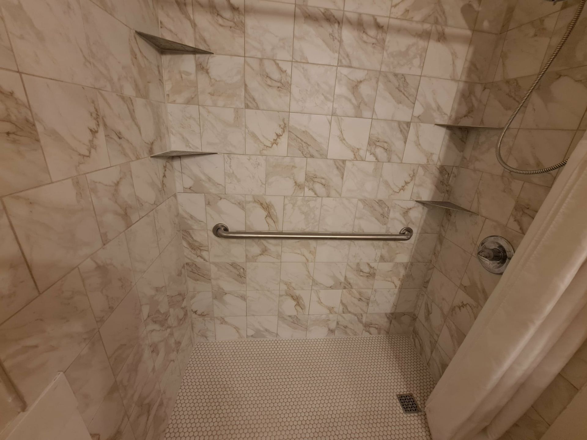 Bathroom shower with tiled walls and floor, built-in shelves, grab bar, and showerhead.