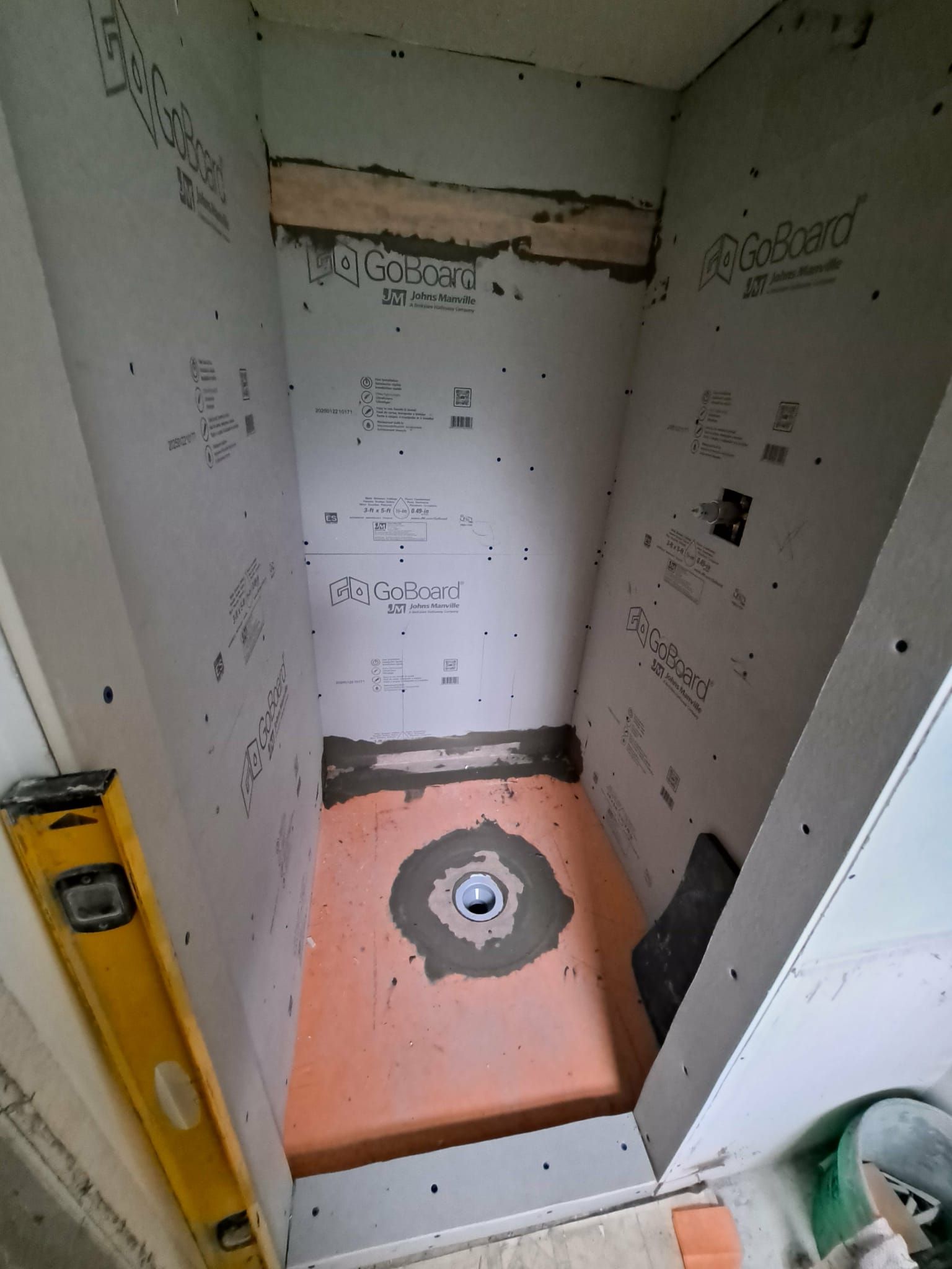 Shower stall under construction, gray walls, orange floor, drain, level, cement.
