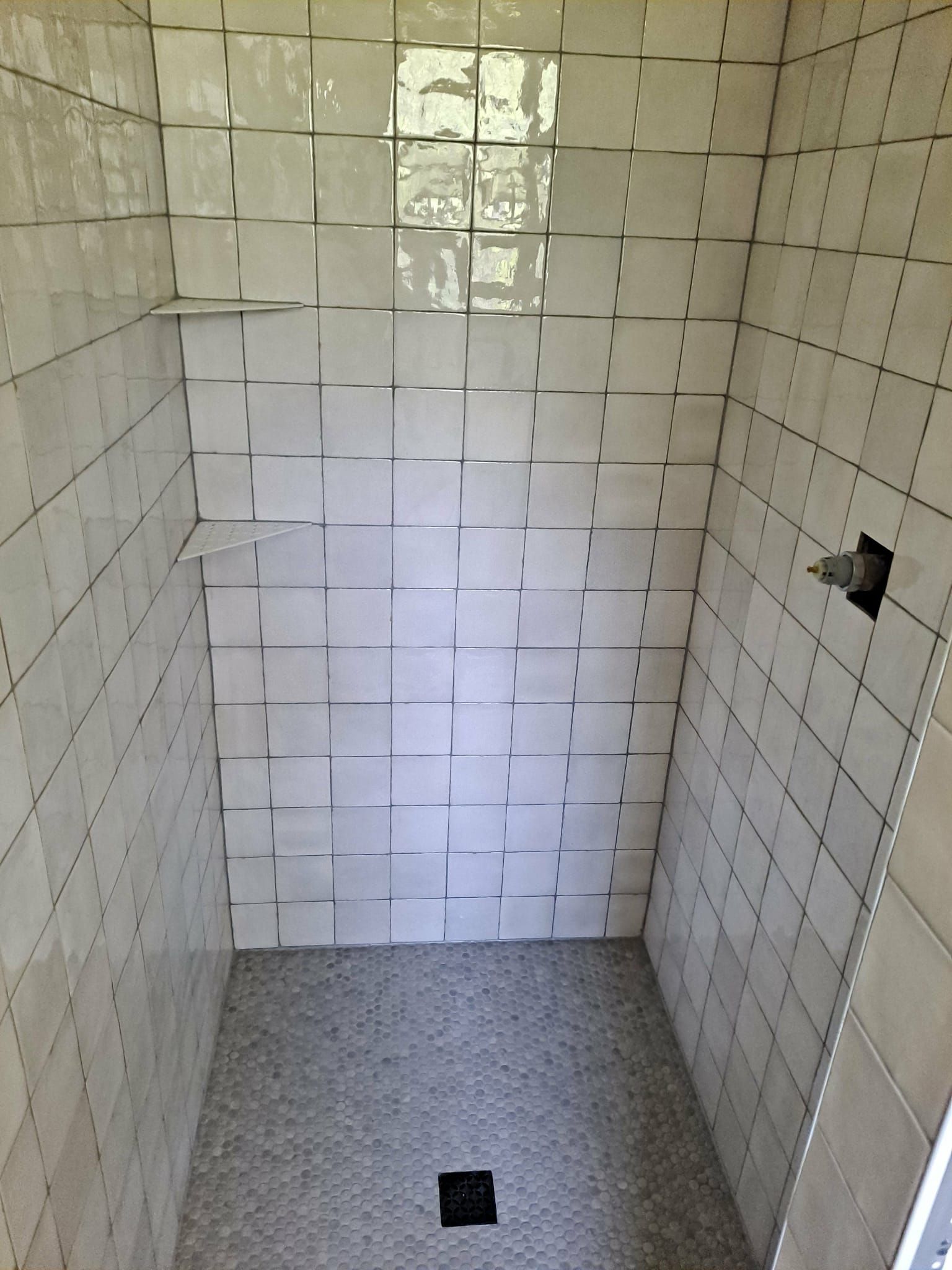 Newly tiled shower stall with white rectangular tiles and a pebble floor.