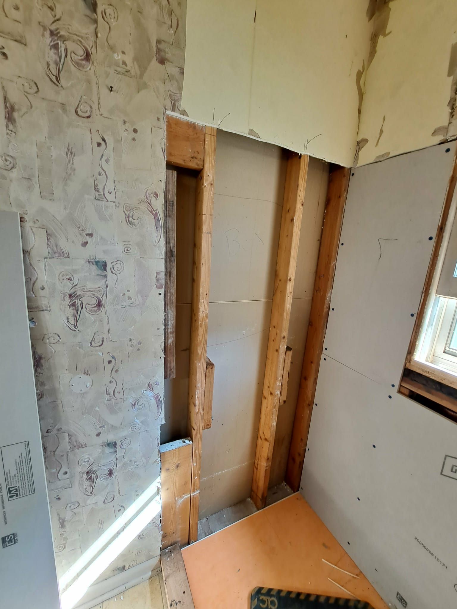 Interior wall studs exposed during renovation, orange floor tile, beige walls, and drywall.