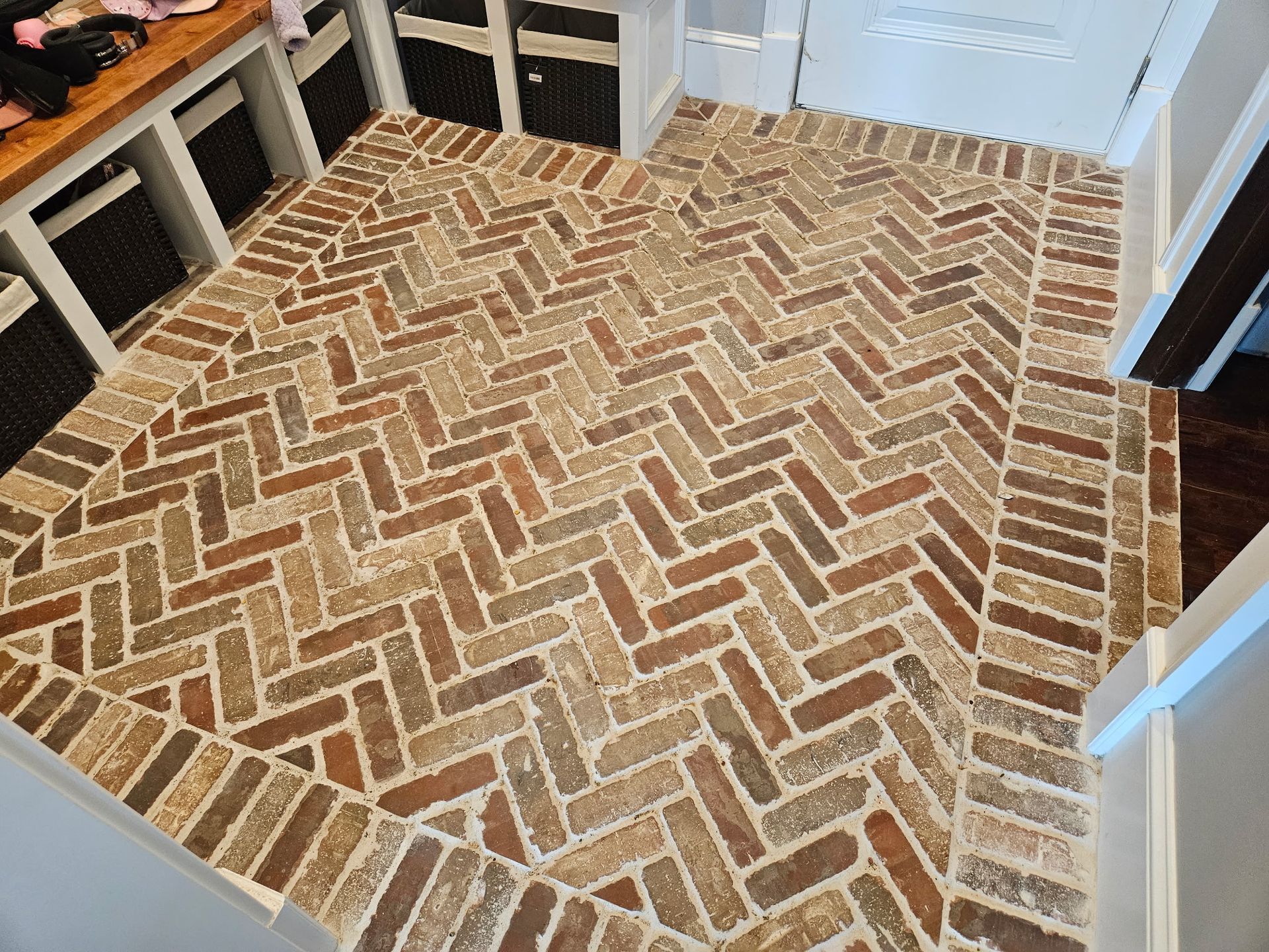Brick herringbone-patterned floor in a room. Border bricks frame the design. Brown and tan colors.