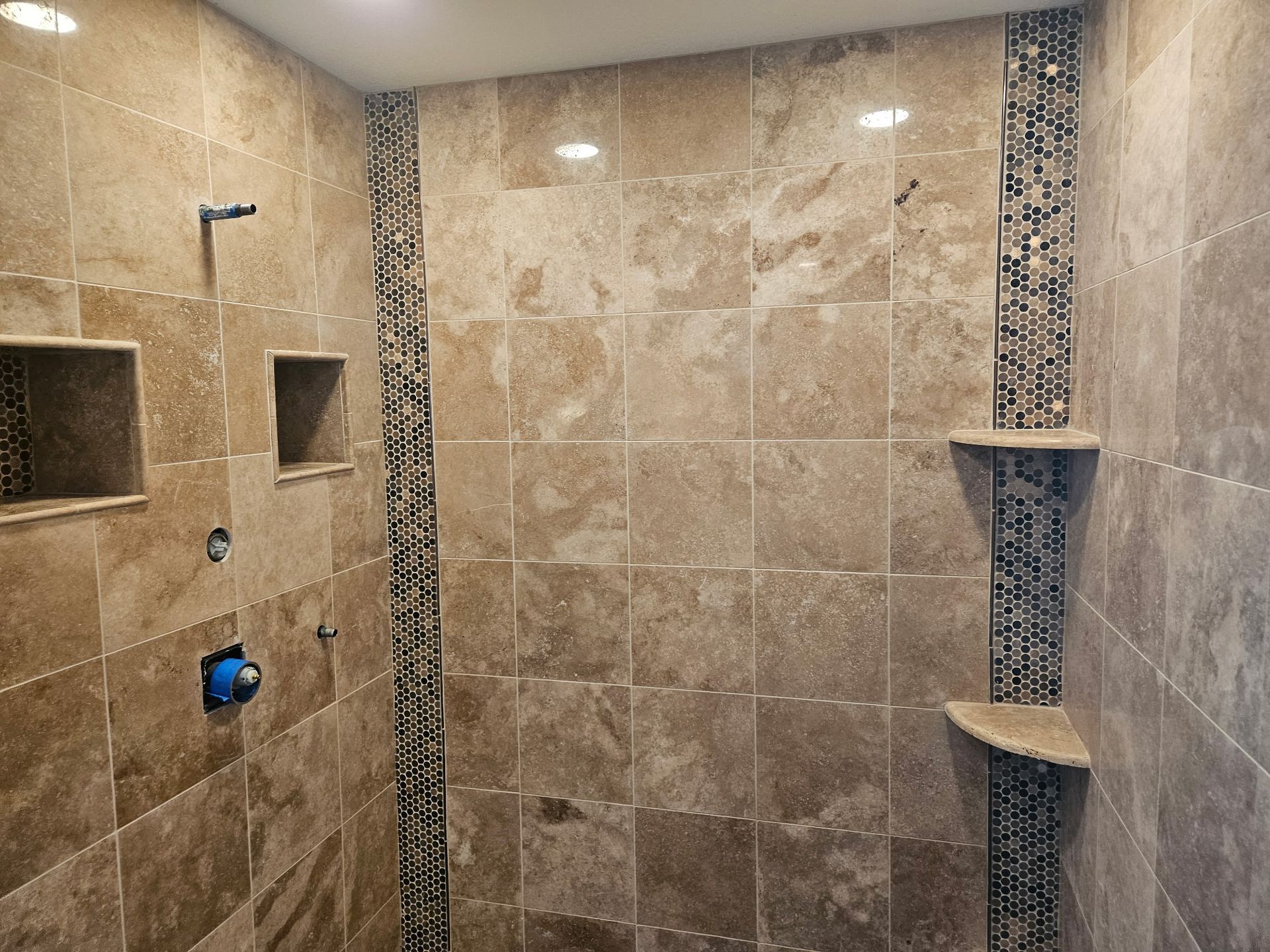 Shower with beige tile walls, mosaic tile accent strip, and built-in shelves.