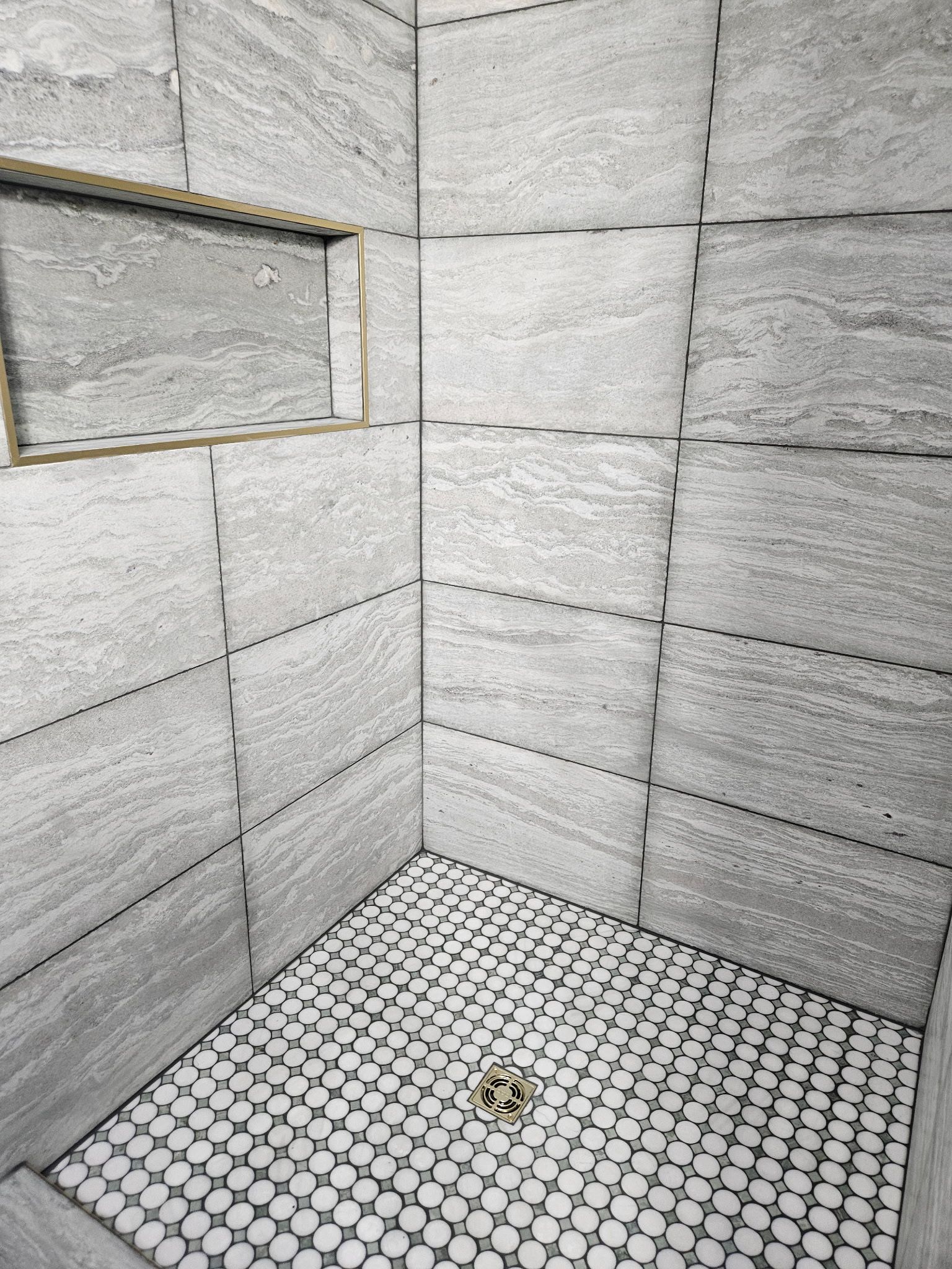 Gray tiled shower with a niche and small patterned floor.