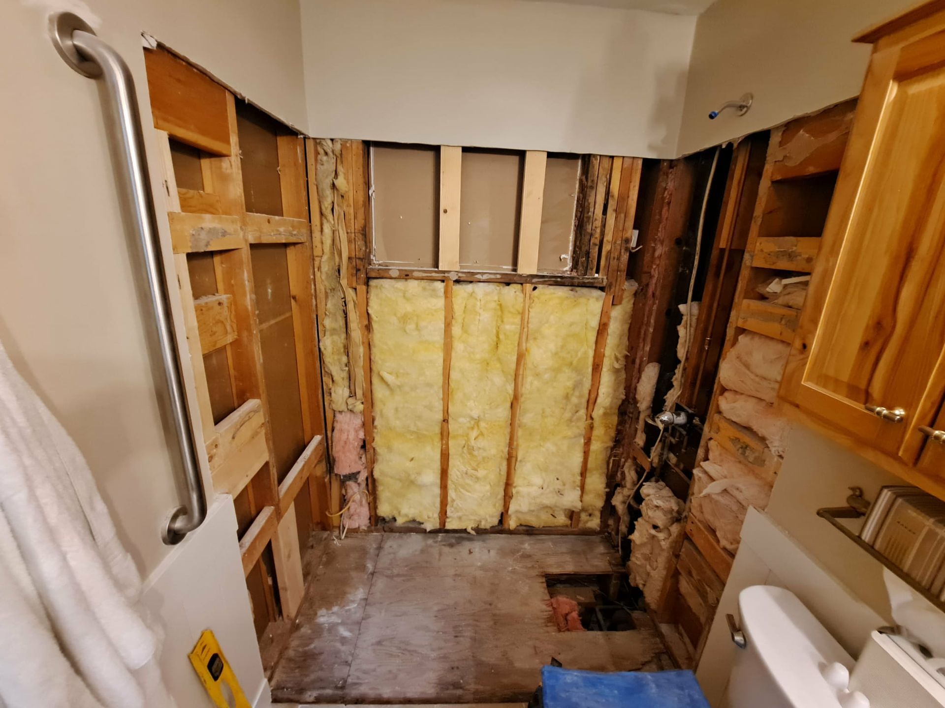 Bathroom renovation in progress, walls open to studs, insulation visible. Handrail, cabinet, and toilet present.