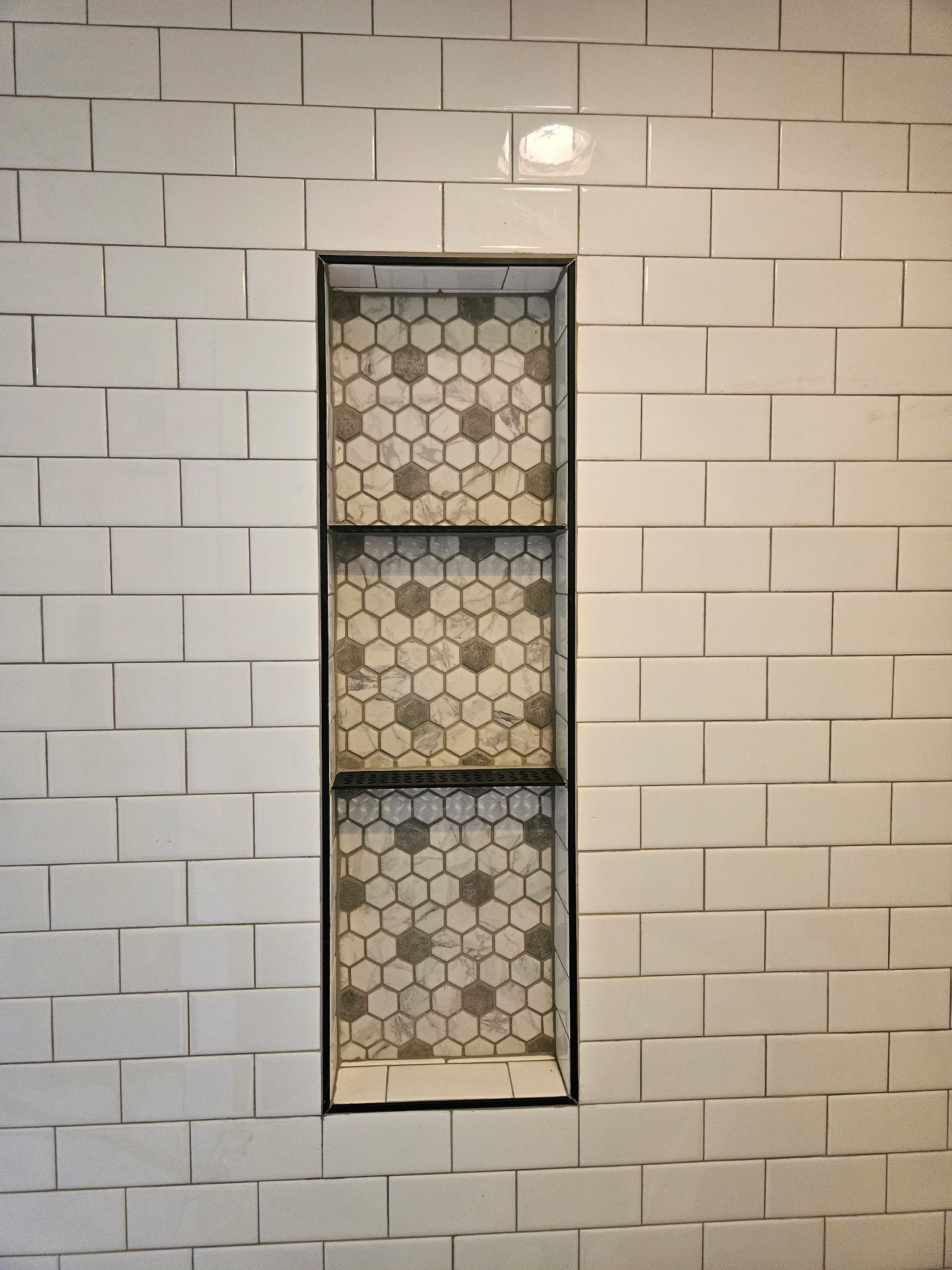 White tiled shower wall with recessed shelving featuring decorative mosaic tile.