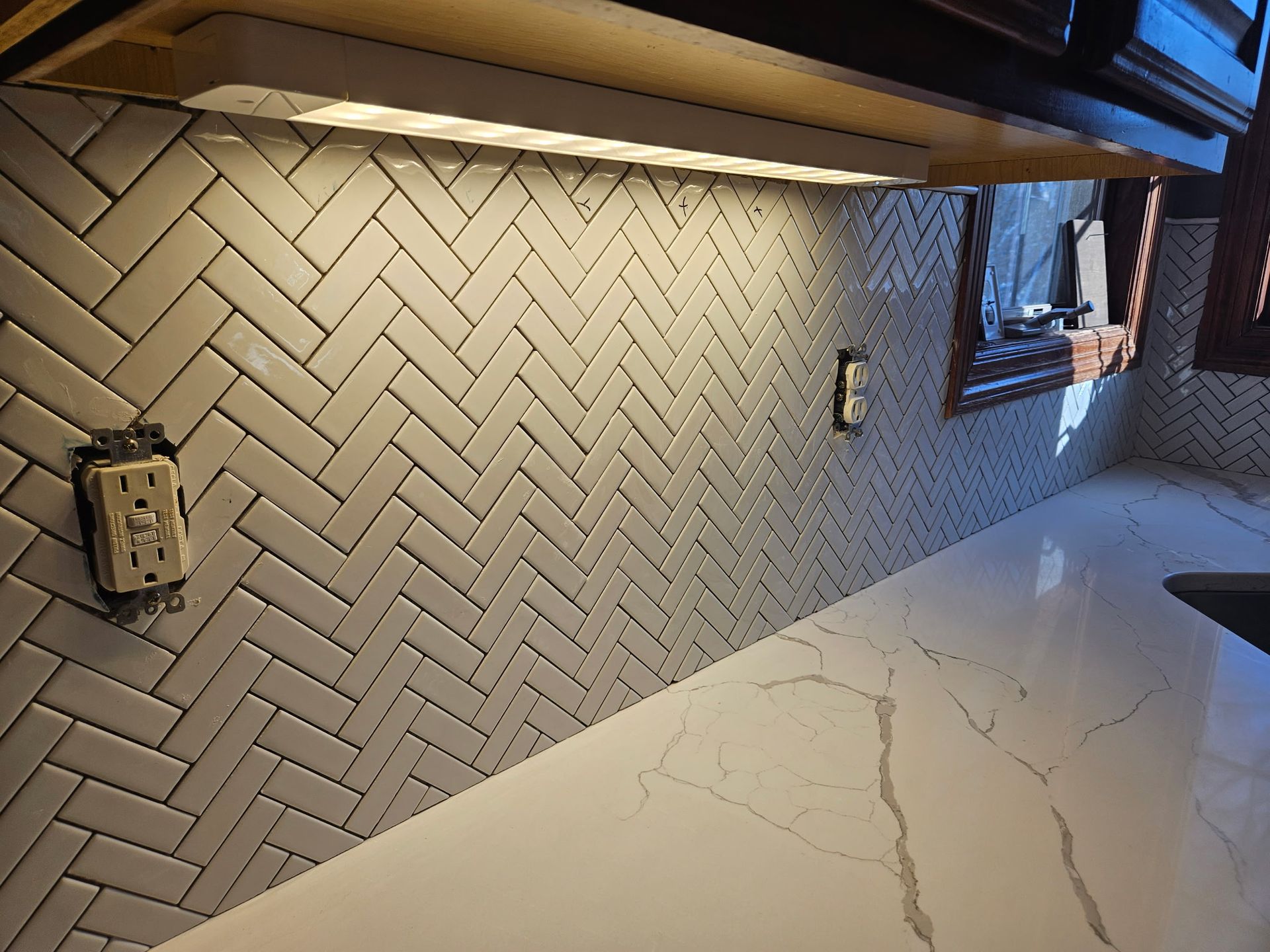 Herringbone tiled backsplash with under-cabinet lighting and a white countertop.