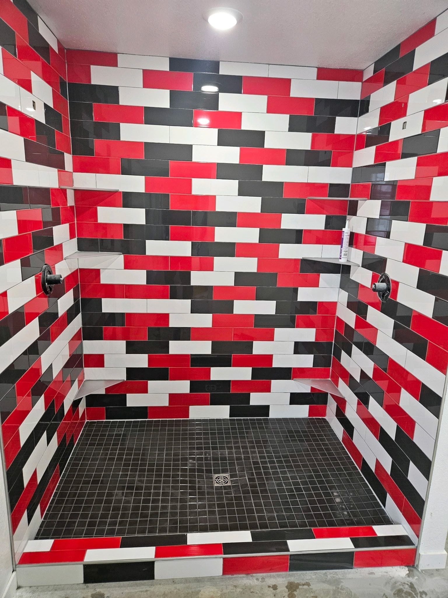 Shower stall with red, black, and white brick-patterned tile walls and floor.