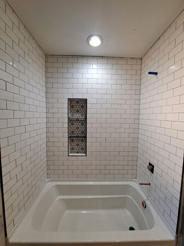 Tiled white shower stall with recessed shelf, white bathtub, overhead light.