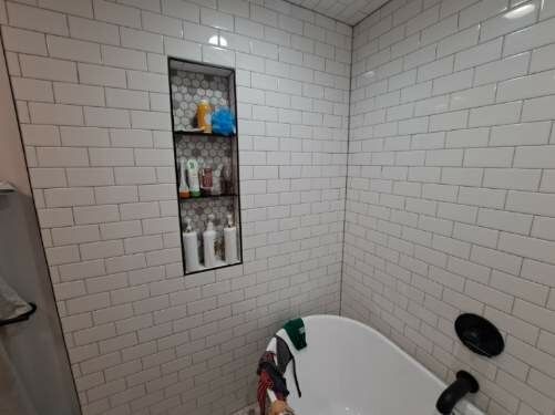 Bathroom with white subway tile walls, a built-in shelf, and a bathtub.
