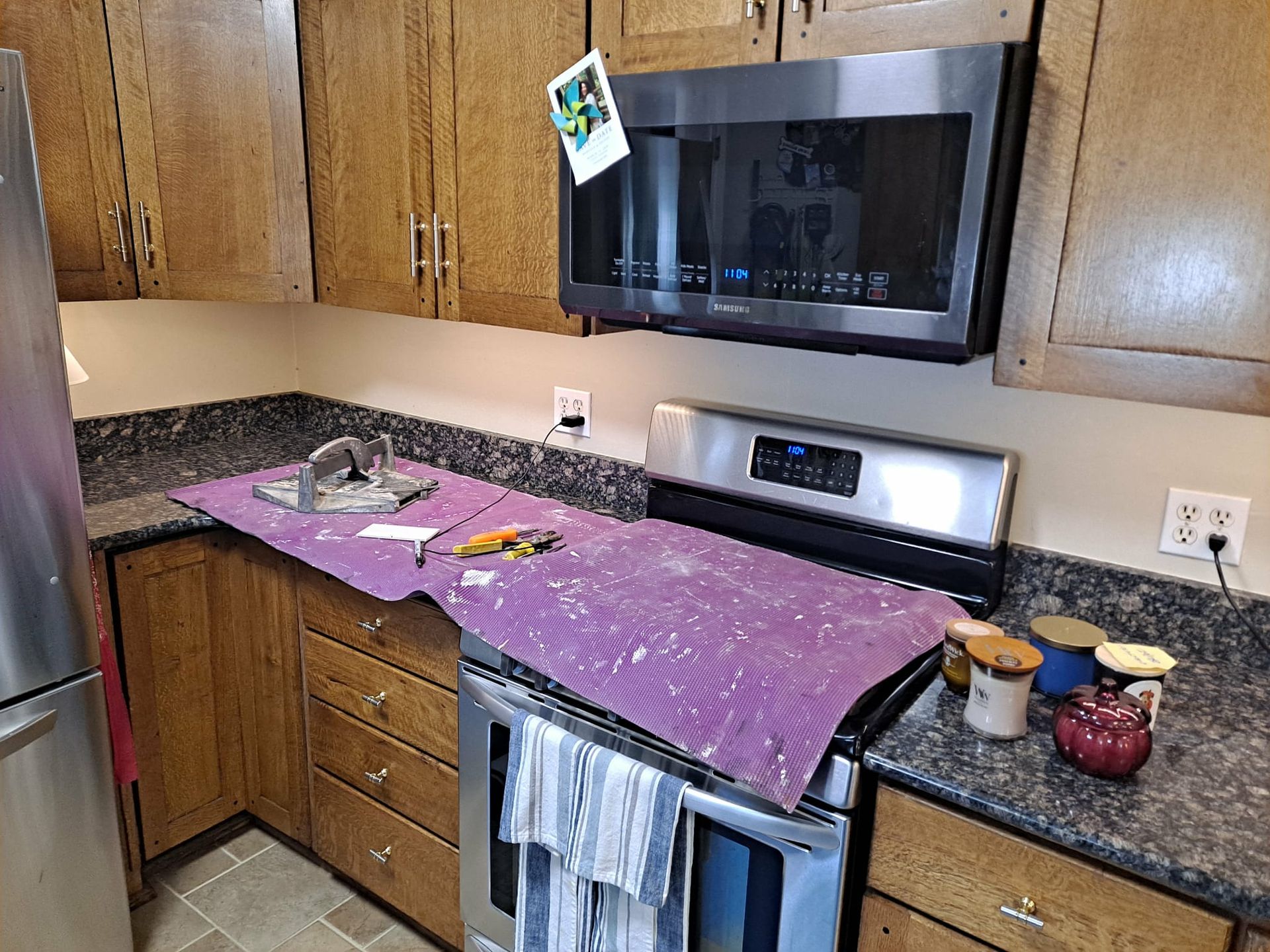 Kitchen with stainless steel appliances, dark wood cabinets, and granite countertops. Tools and protective mat sit on the stove.