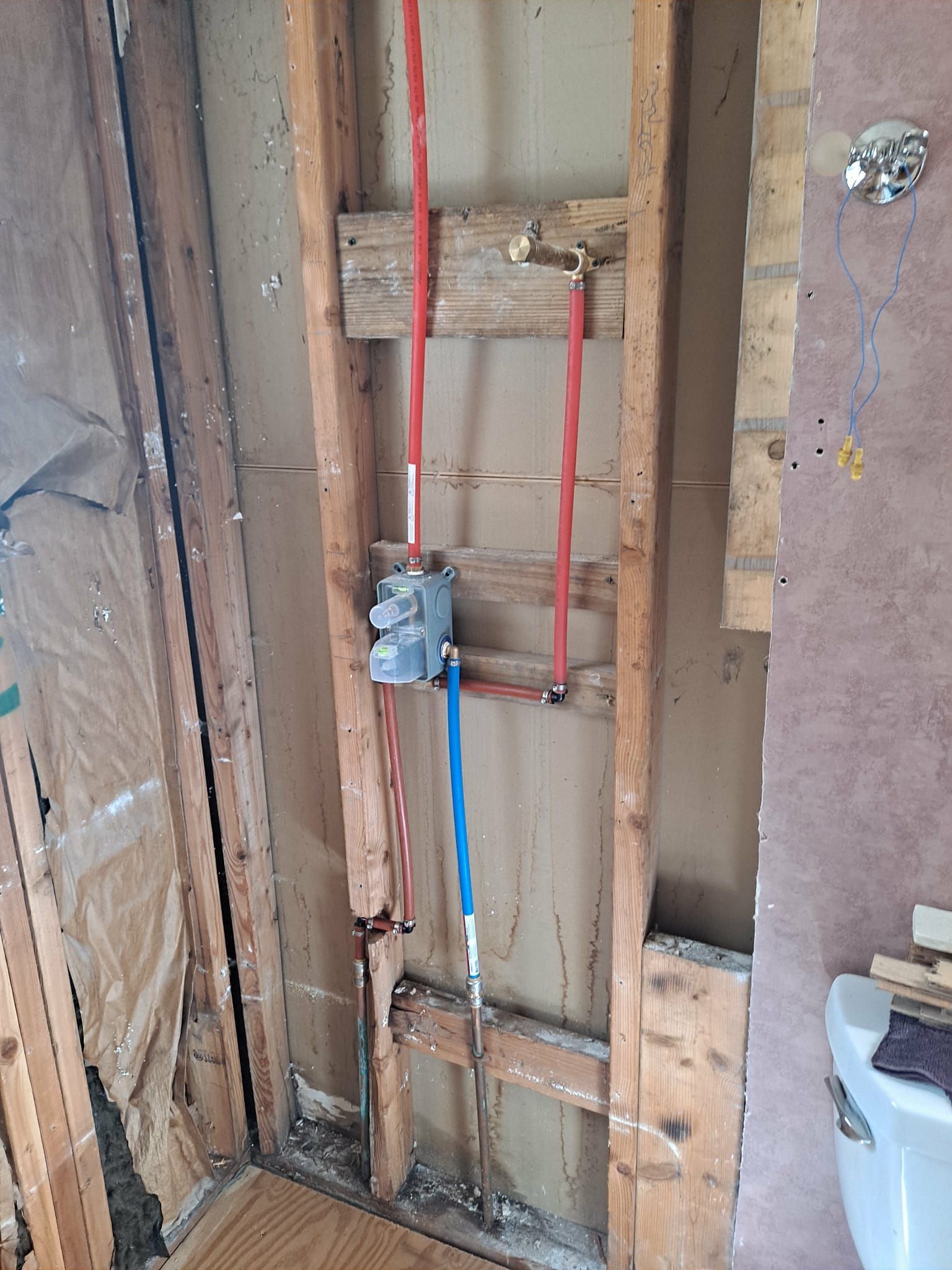 Framed wall with exposed plumbing for a shower. Red and blue pipes are visible, along with a valve.