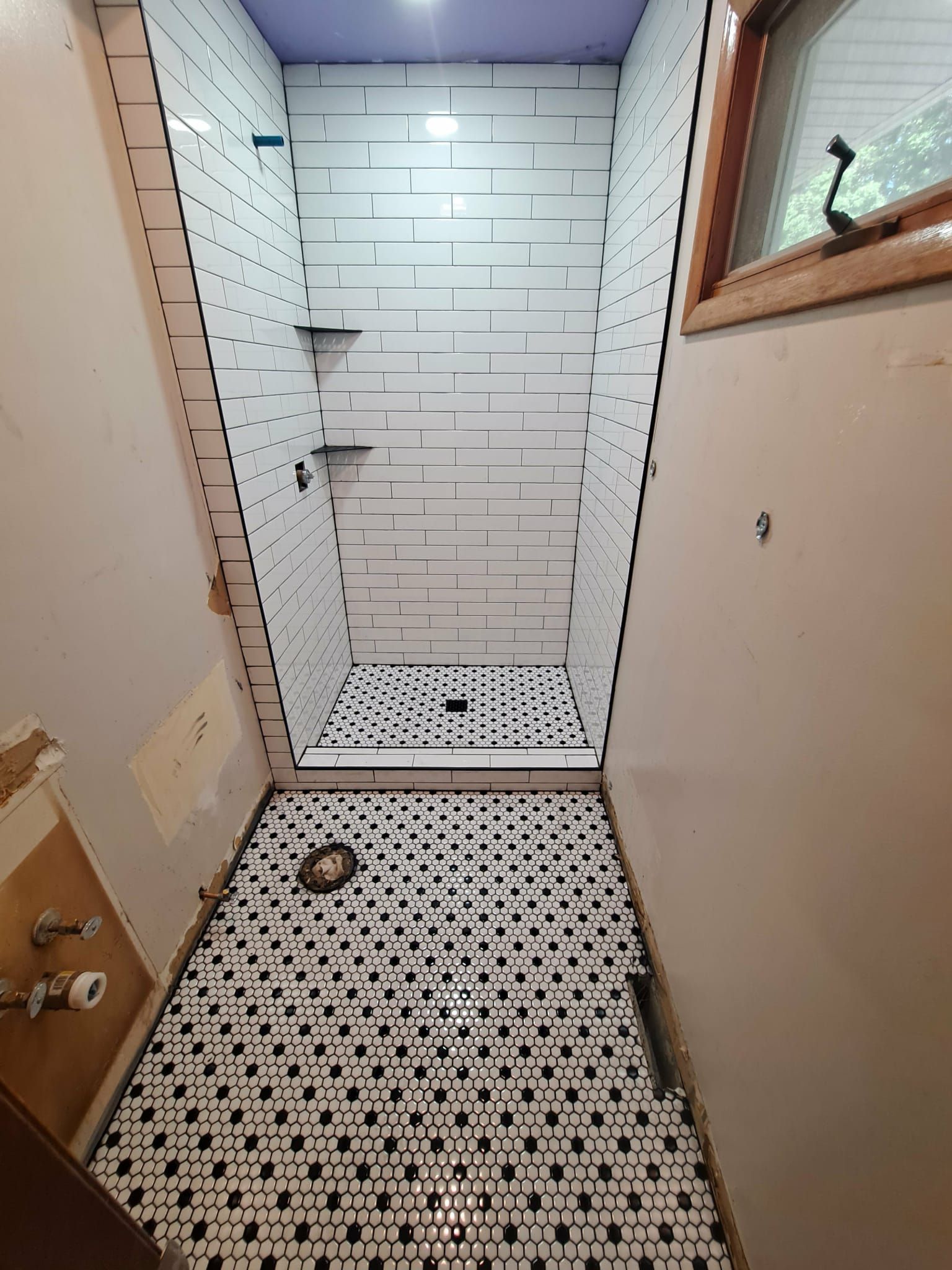 Narrow bathroom under construction, tiled with white and black patterns. Walls are white, awaiting finish.