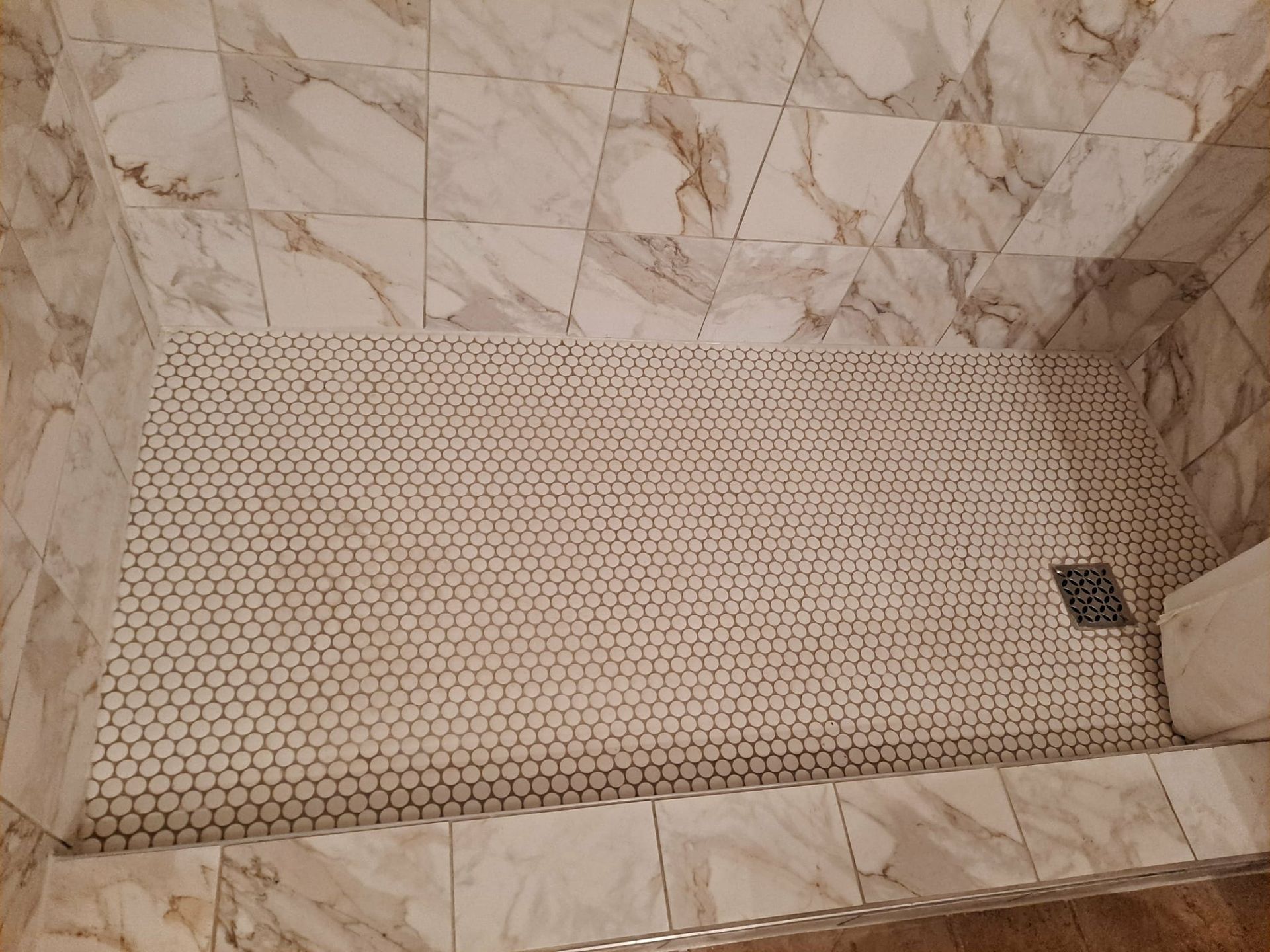 Shower with marble-patterned walls and hexagonal tile floor. Drain in corner.
