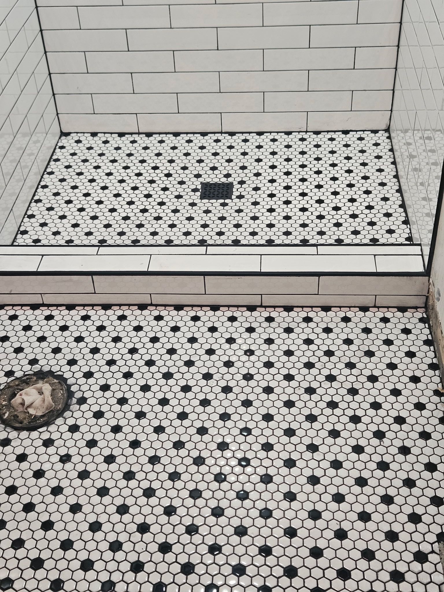 Black and white tiled shower floor with ornate drain and mosaic pattern.