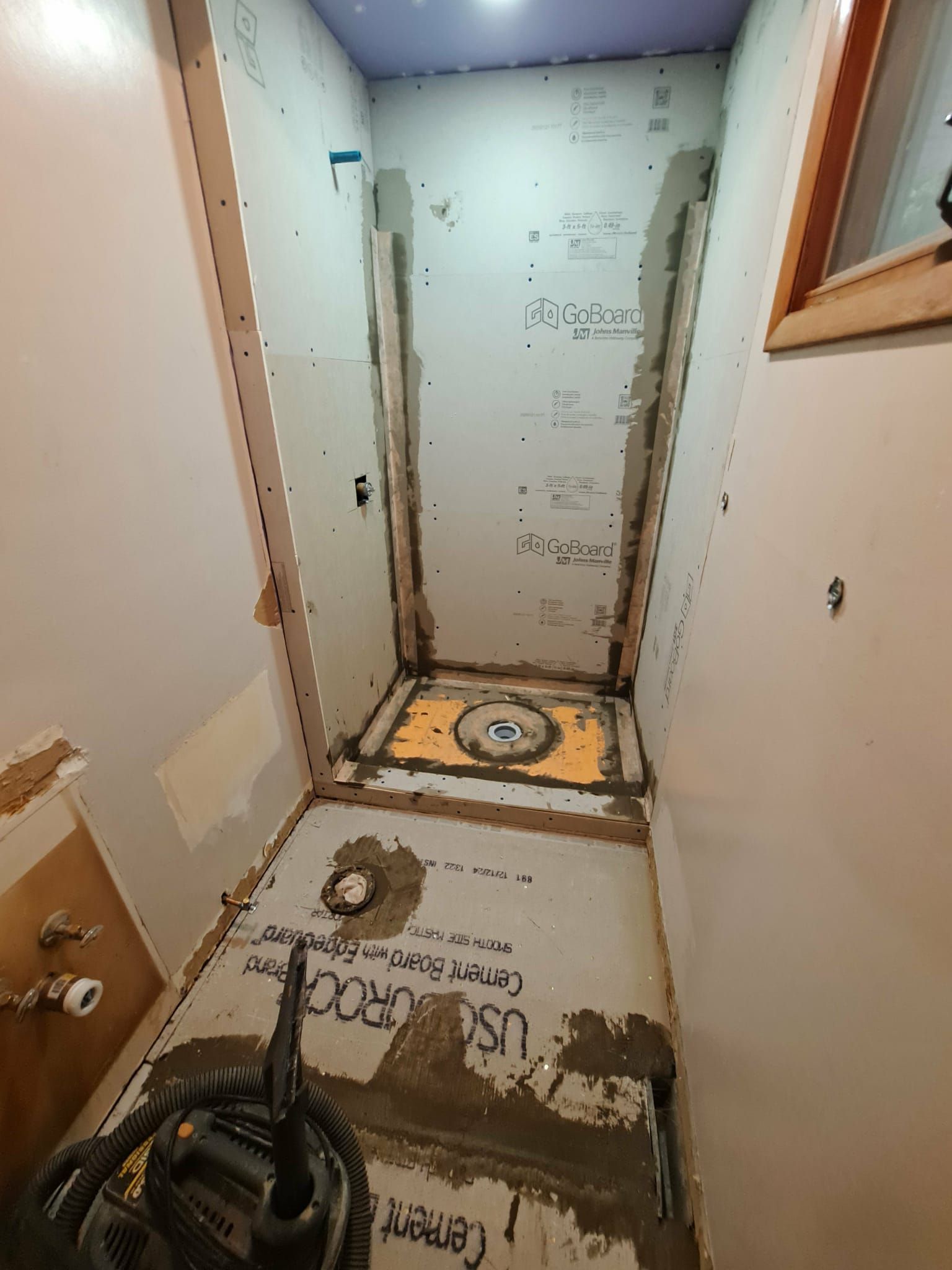 Bathroom renovation in progress, shower stall framed with cement board, floor drain visible, walls partially finished.