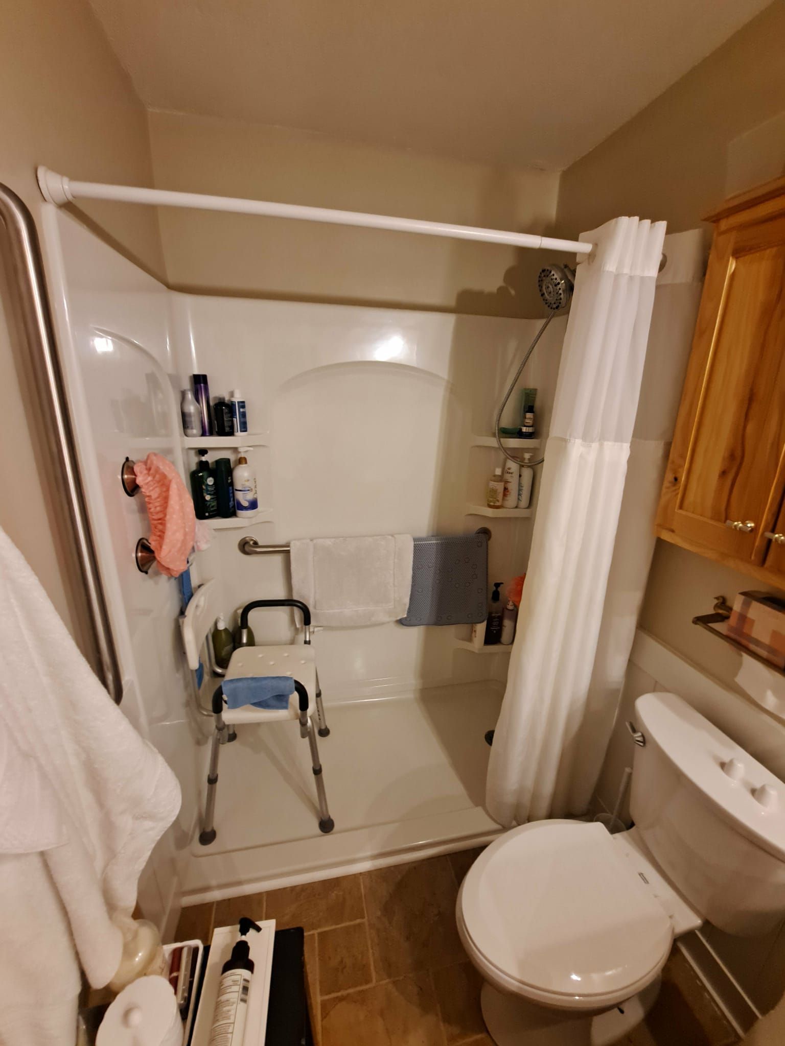 White shower stall with seat, grab bar, and curtain next to toilet.