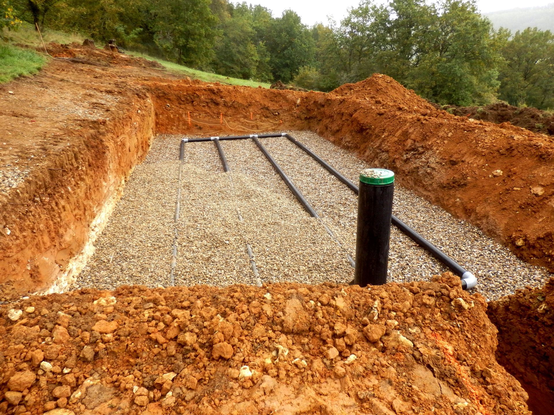 Excavated rectangular trench filled with gravel and black pipes, part of a septic system.