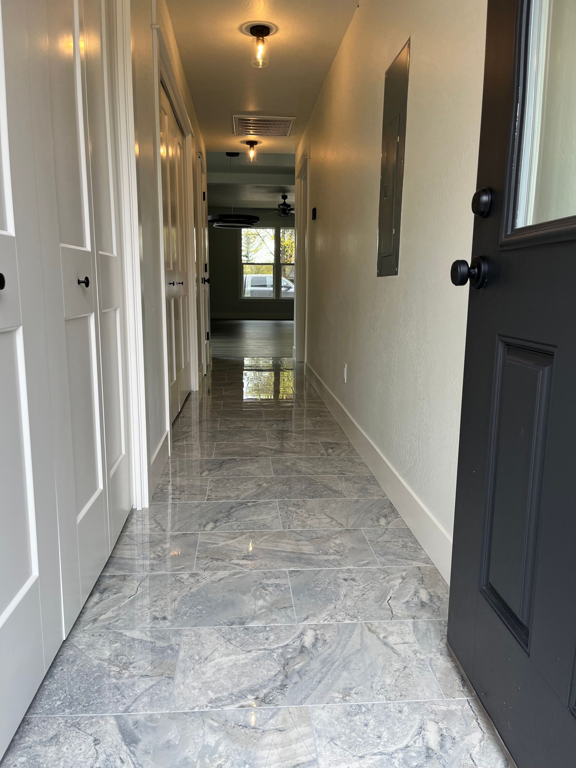 Narrow hallway with glossy gray tile floor, white walls, and an open black front door.