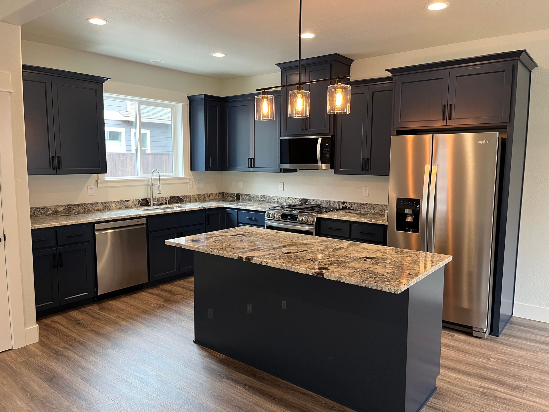 Modern kitchen with dark cabinets, granite island, stainless steel fridge, and pendant lights