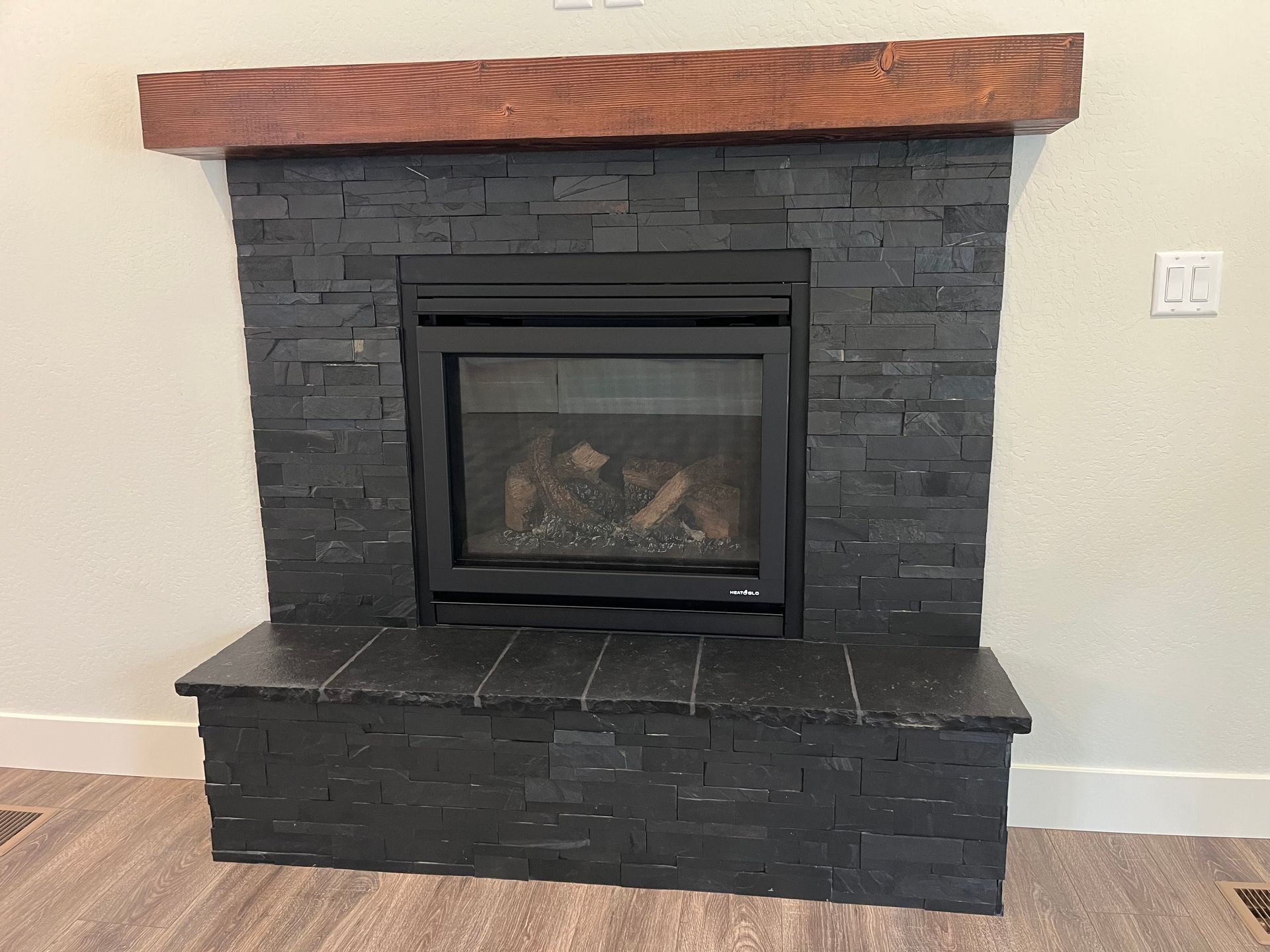 Modern black stone fireplace with wood mantel and surround in a light-colored room