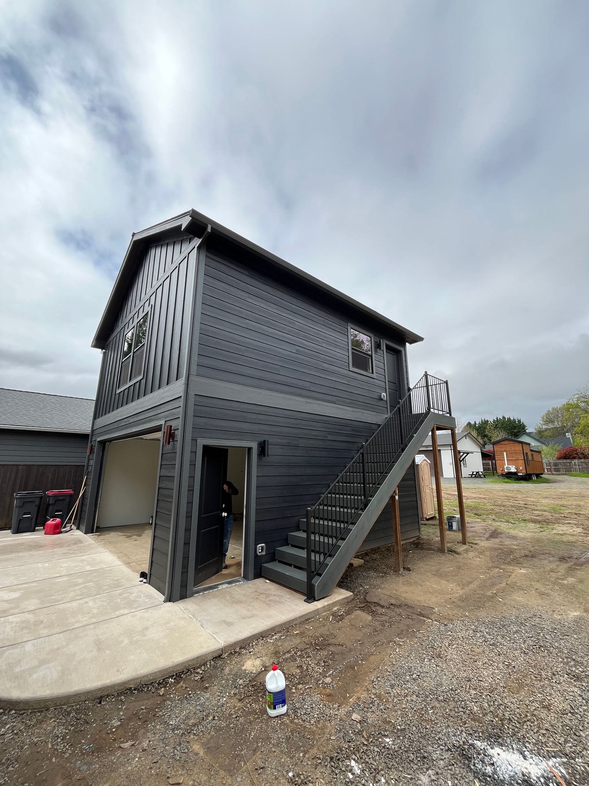 Black metal building with exterior stairs and a paved area under a cloudy sky