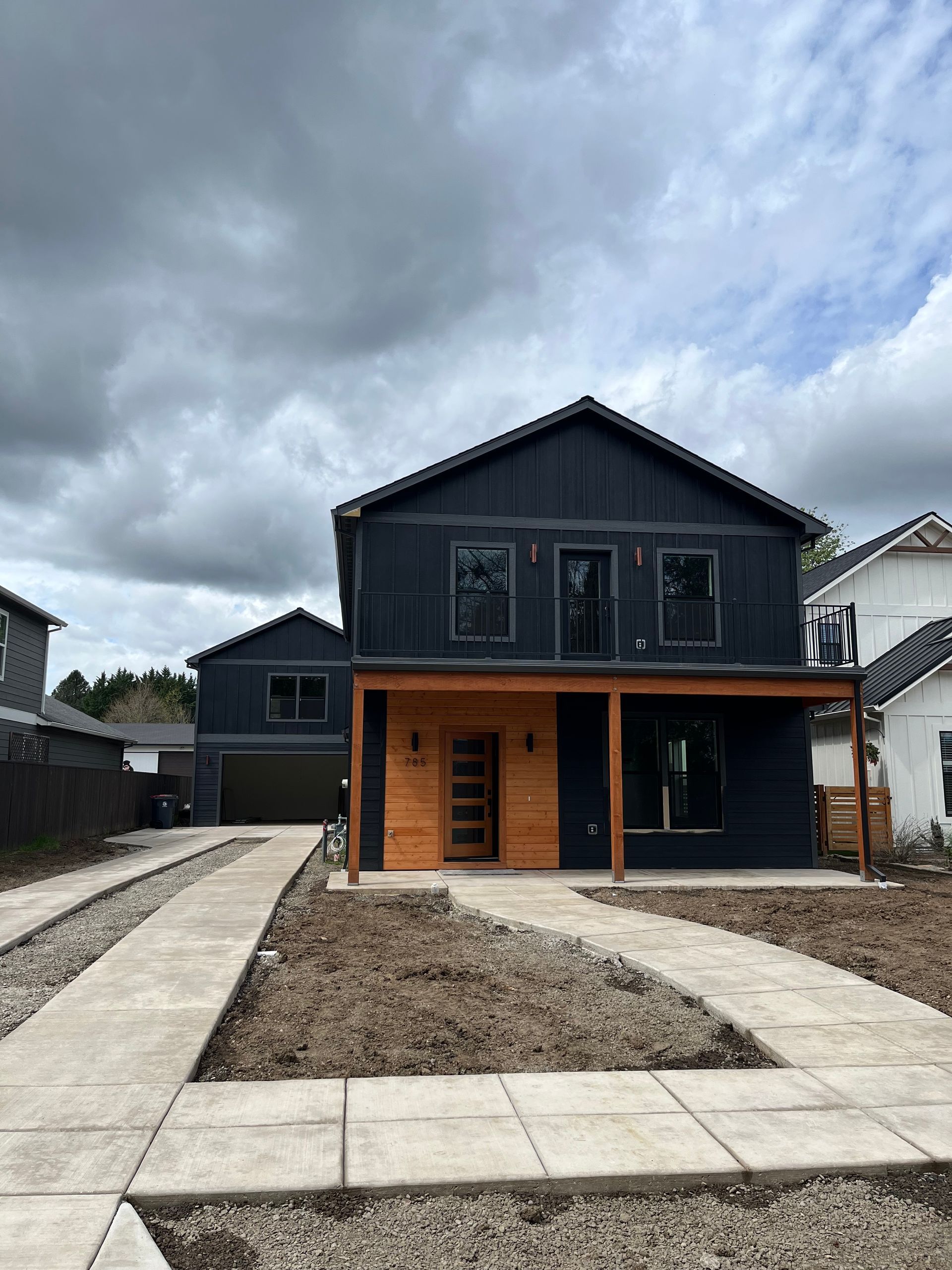 Modern two-story dark house with wood accents, a driveway, and a cloudy sky.