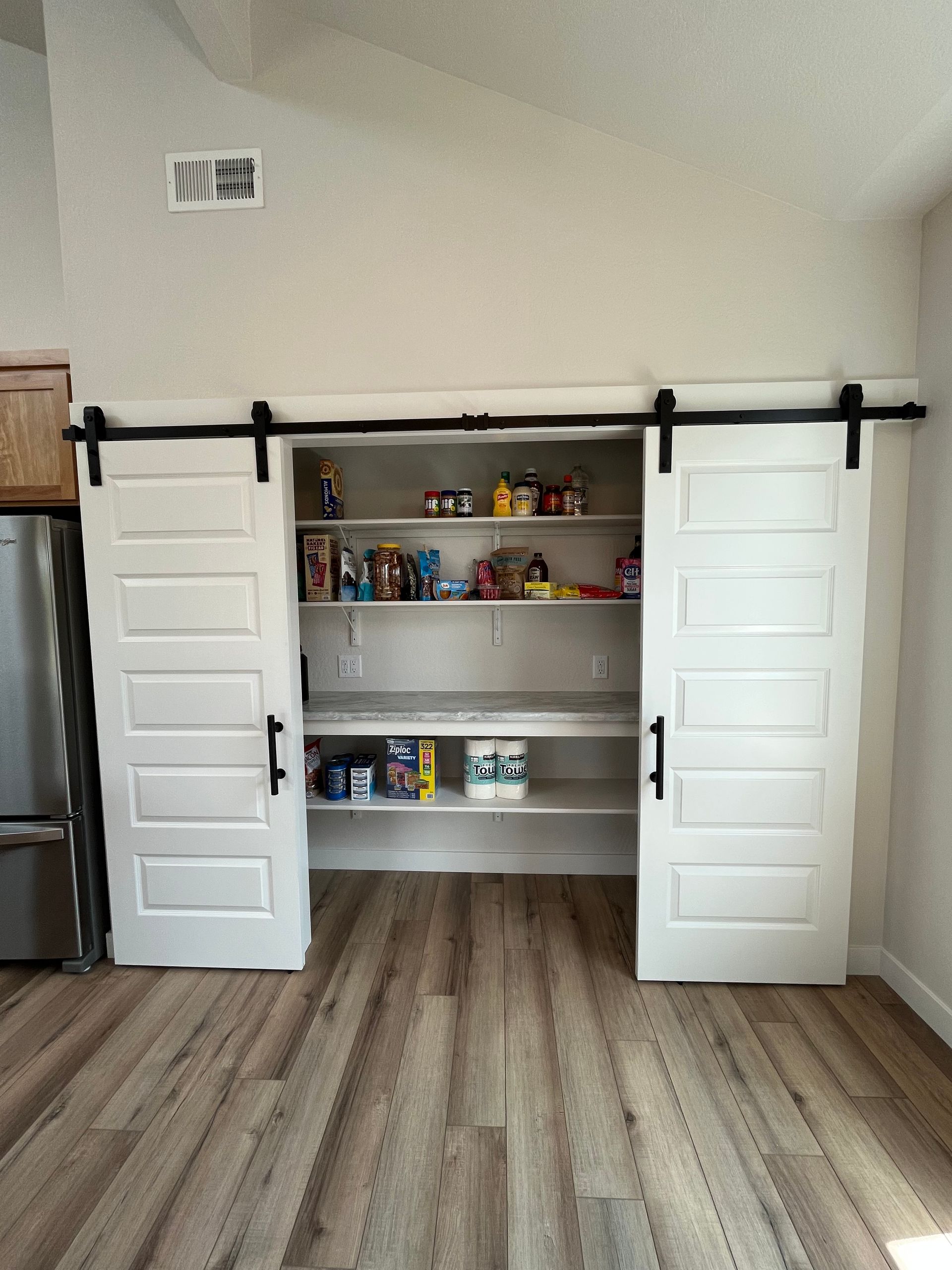 Closet with white sliding doors open, showing shelves stocked with toys and items in a room with wood flooring.