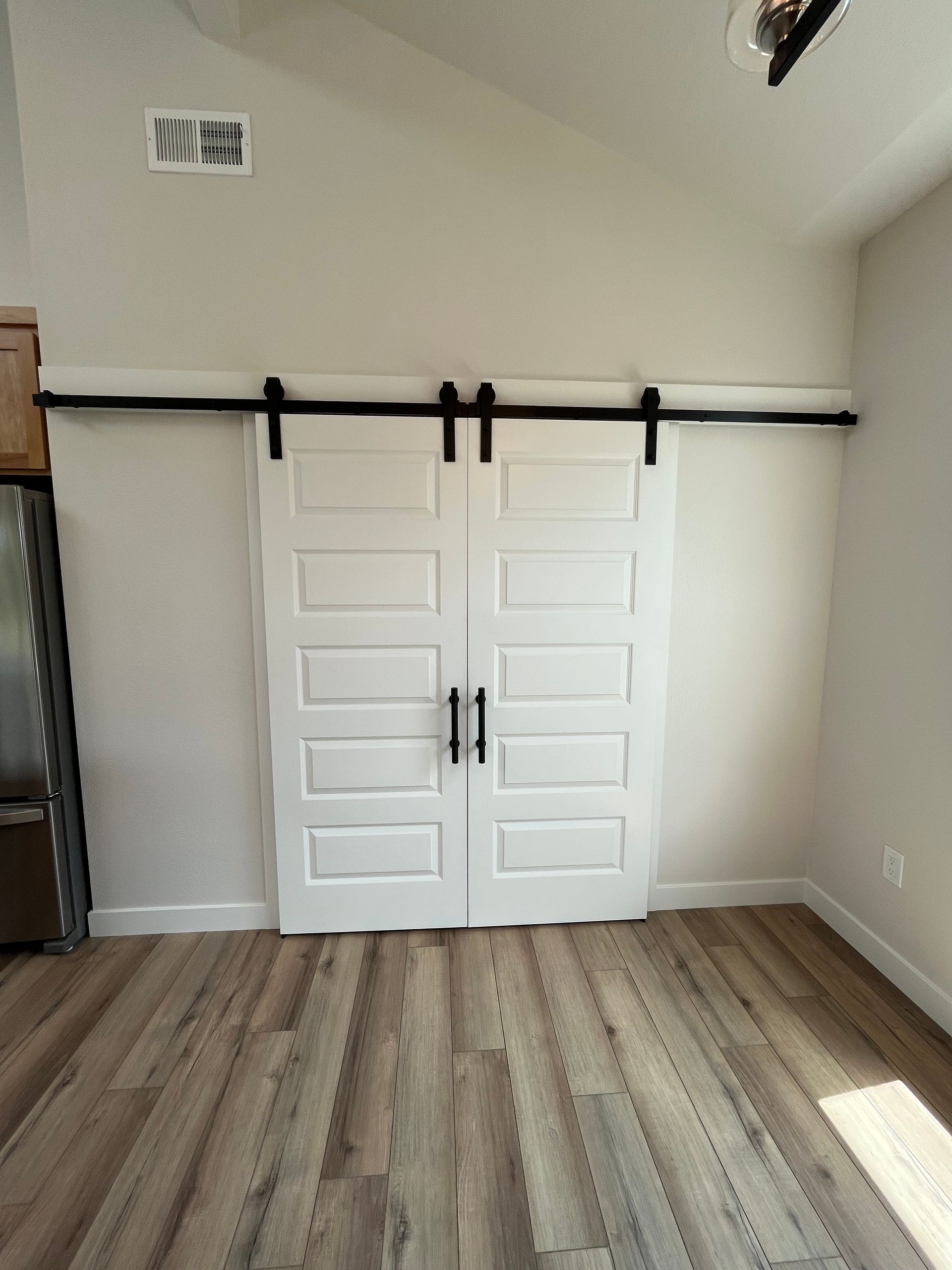 White barn doors with black sliding hardware in a bright room with wood flooring