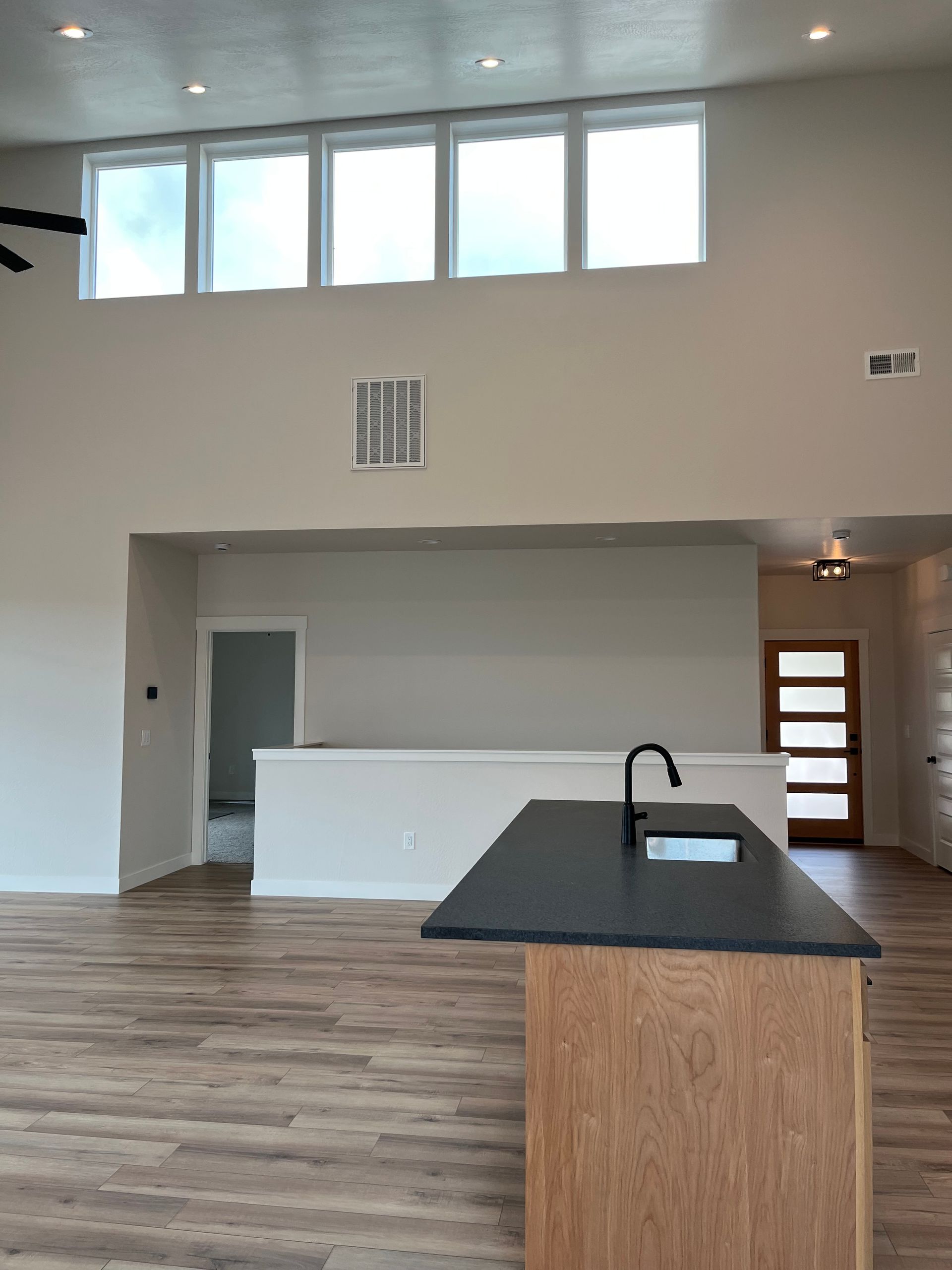 Bright modern kitchen and living area with white walls, wood floors, large windows, and a black island countertop