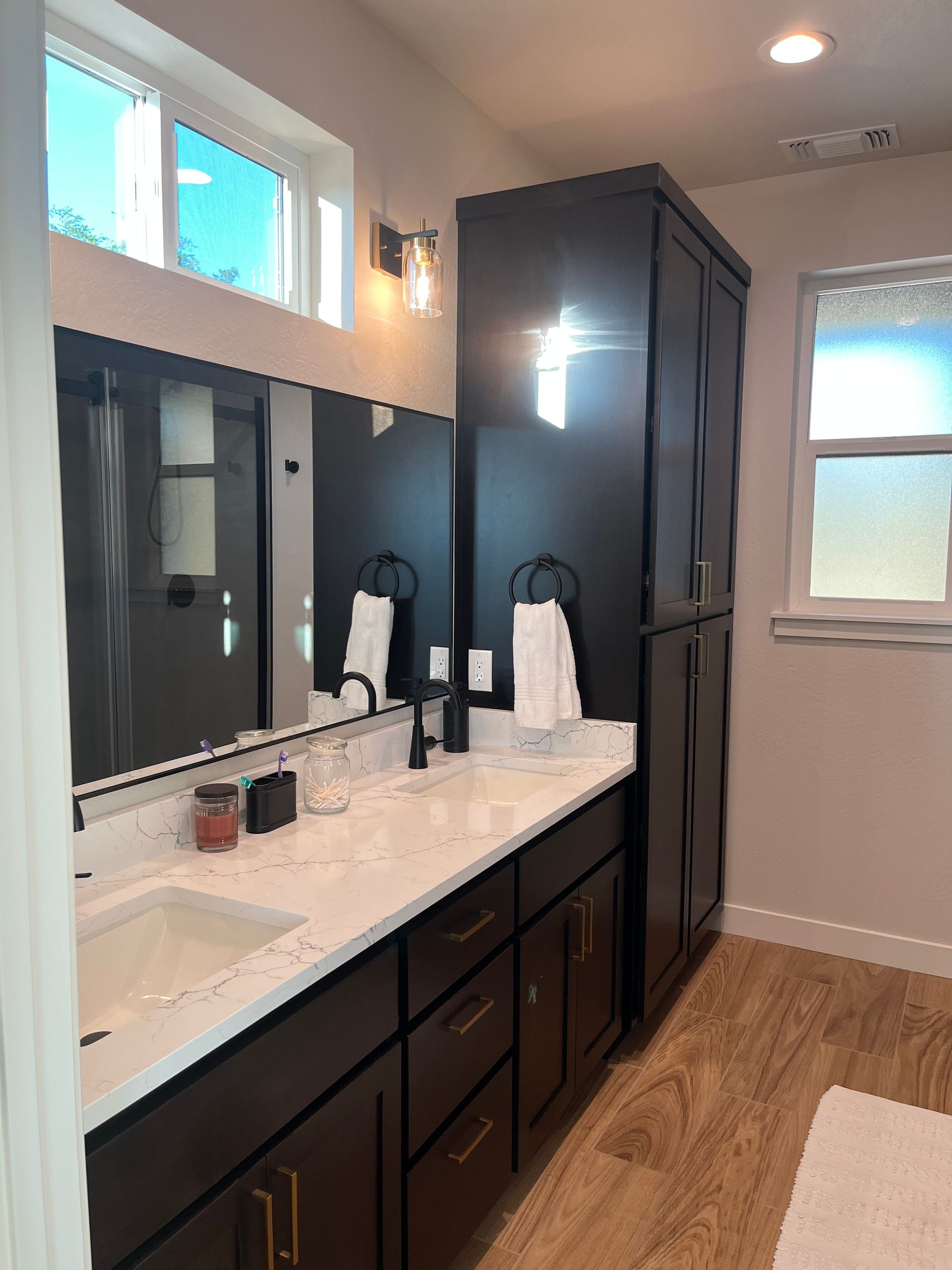 Modern bathroom with double vanity, dark cabinets, black shower curtain, and light wood floor