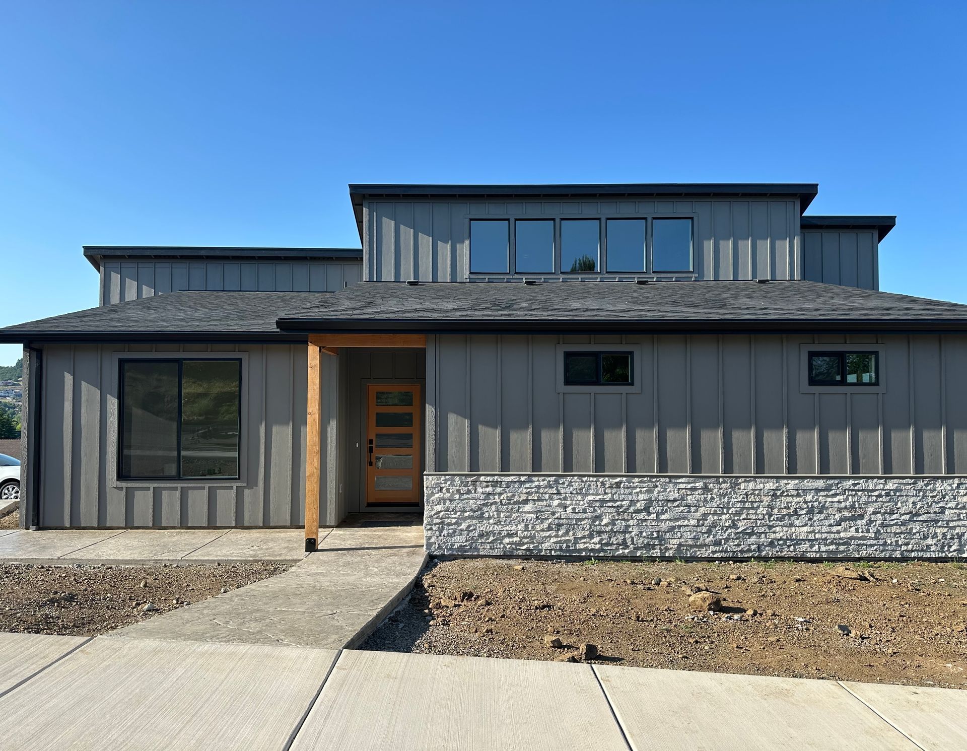 Modern gray house exterior with stone accents, front walkway, and landscaped yard under a blue sky