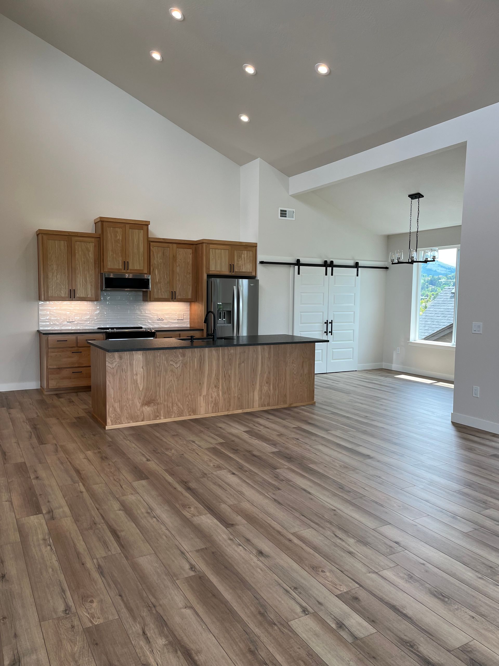 Empty modern kitchen and living area with wood floors, white walls, and island