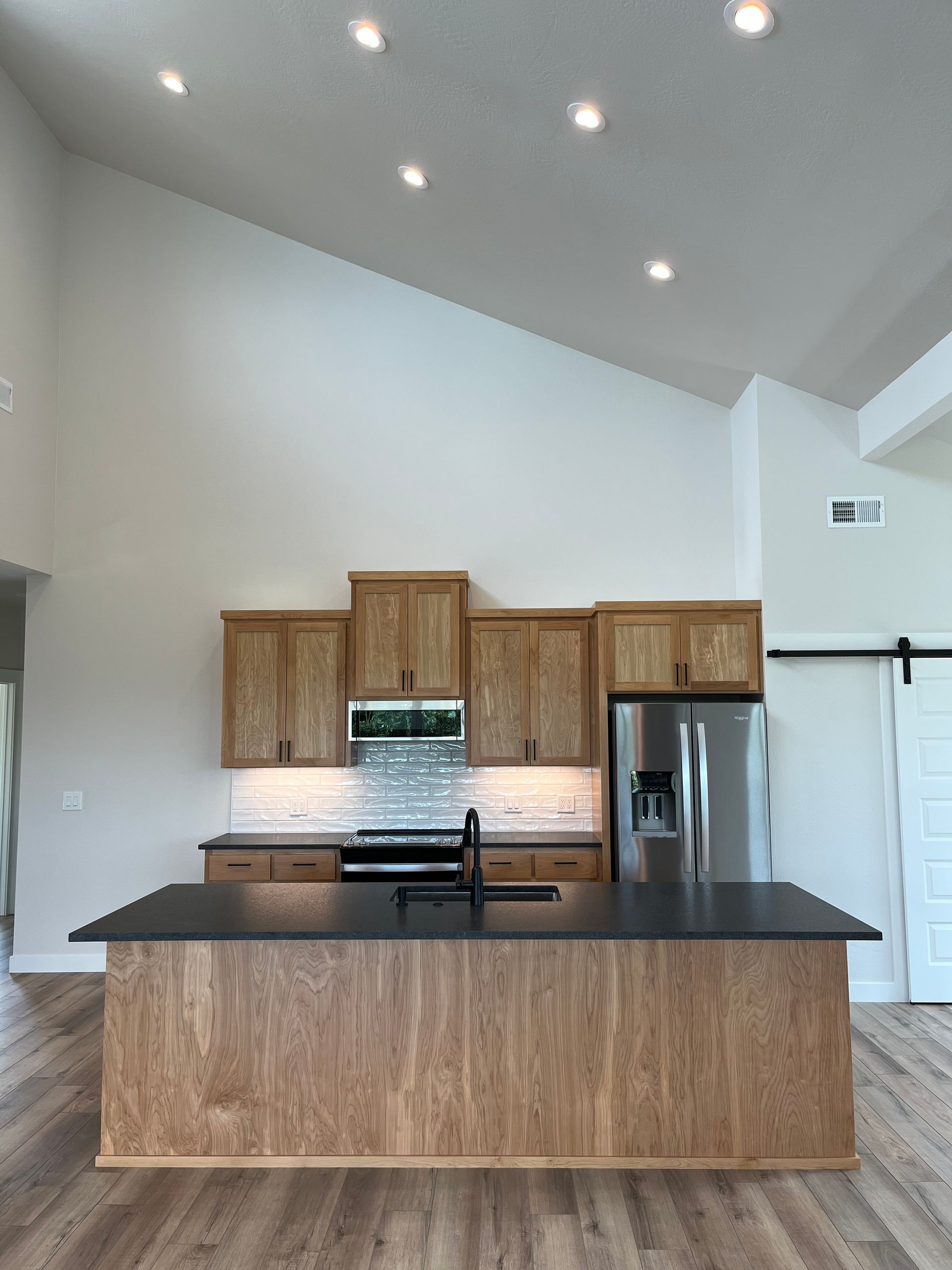 Modern kitchen with wood cabinets, black island countertop, stainless fridge, and high vaulted ceiling