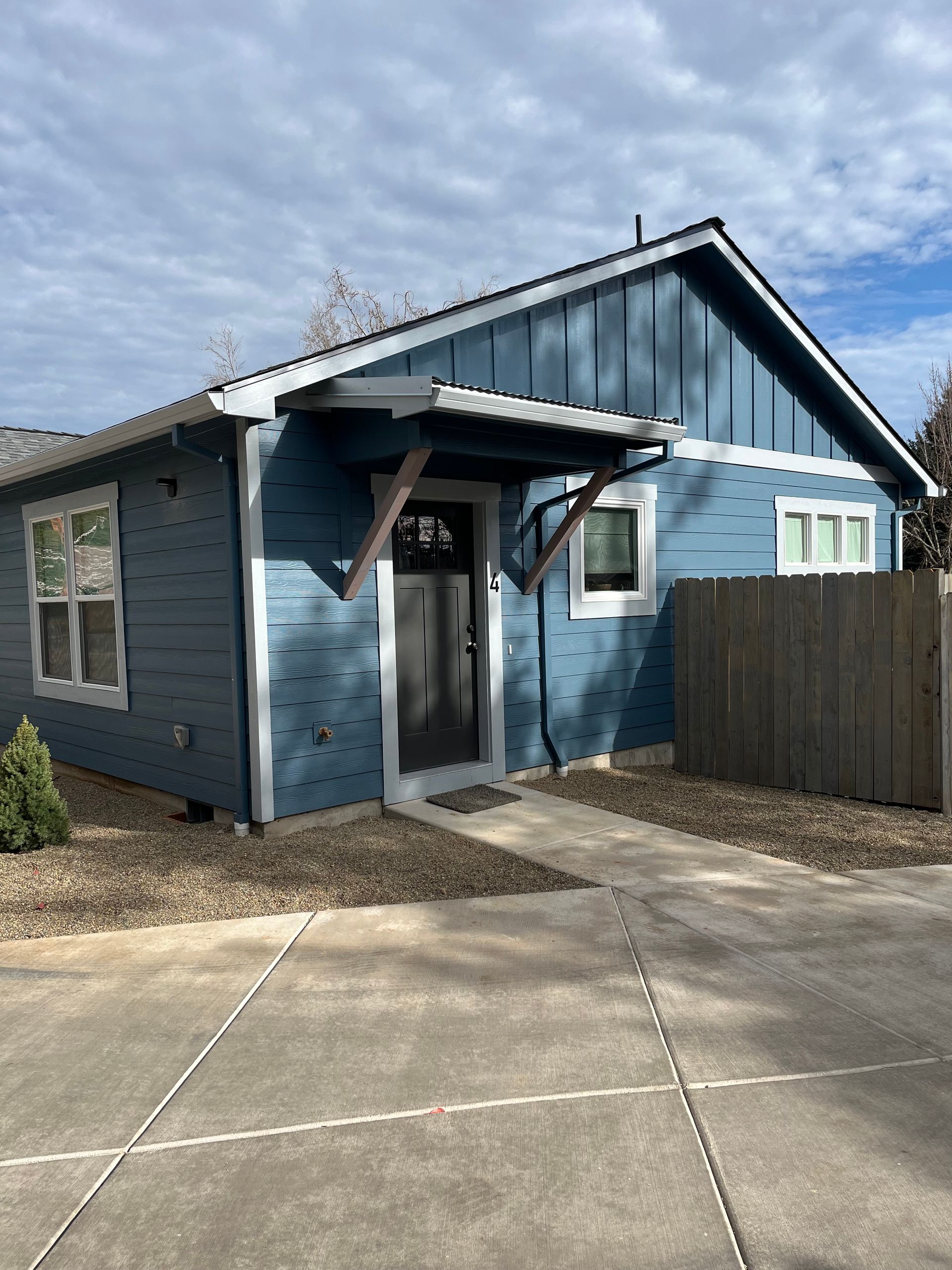 Blue house exterior with a small covered porch, fenced yard, and concrete driveway under a cloudy sky
