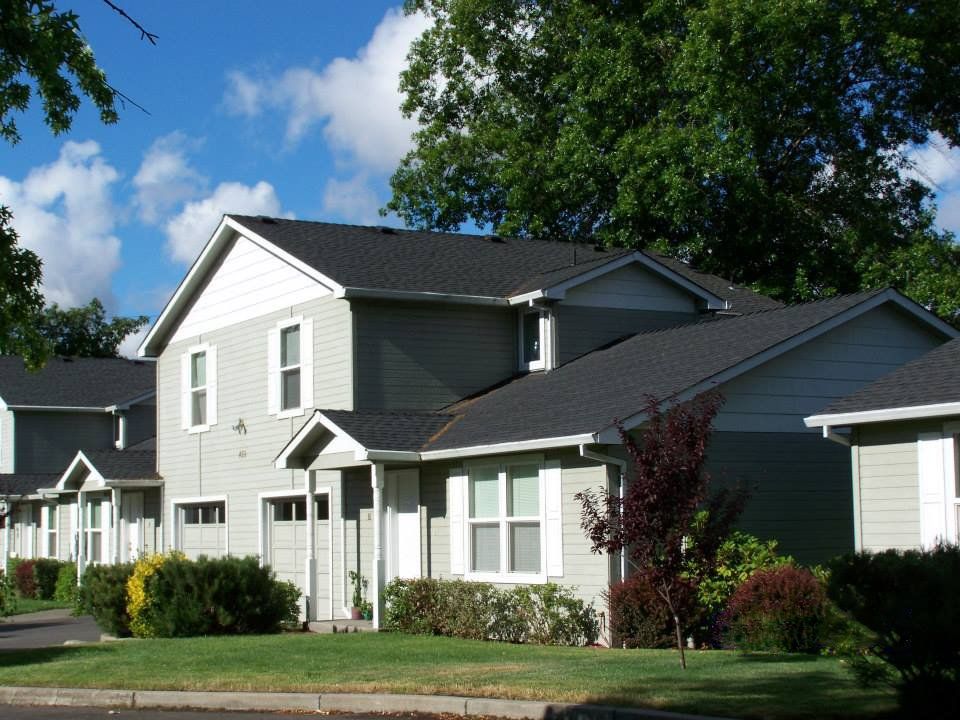 Suburban two-story house with white siding, dark roof, and a green lawn under a blue sky
