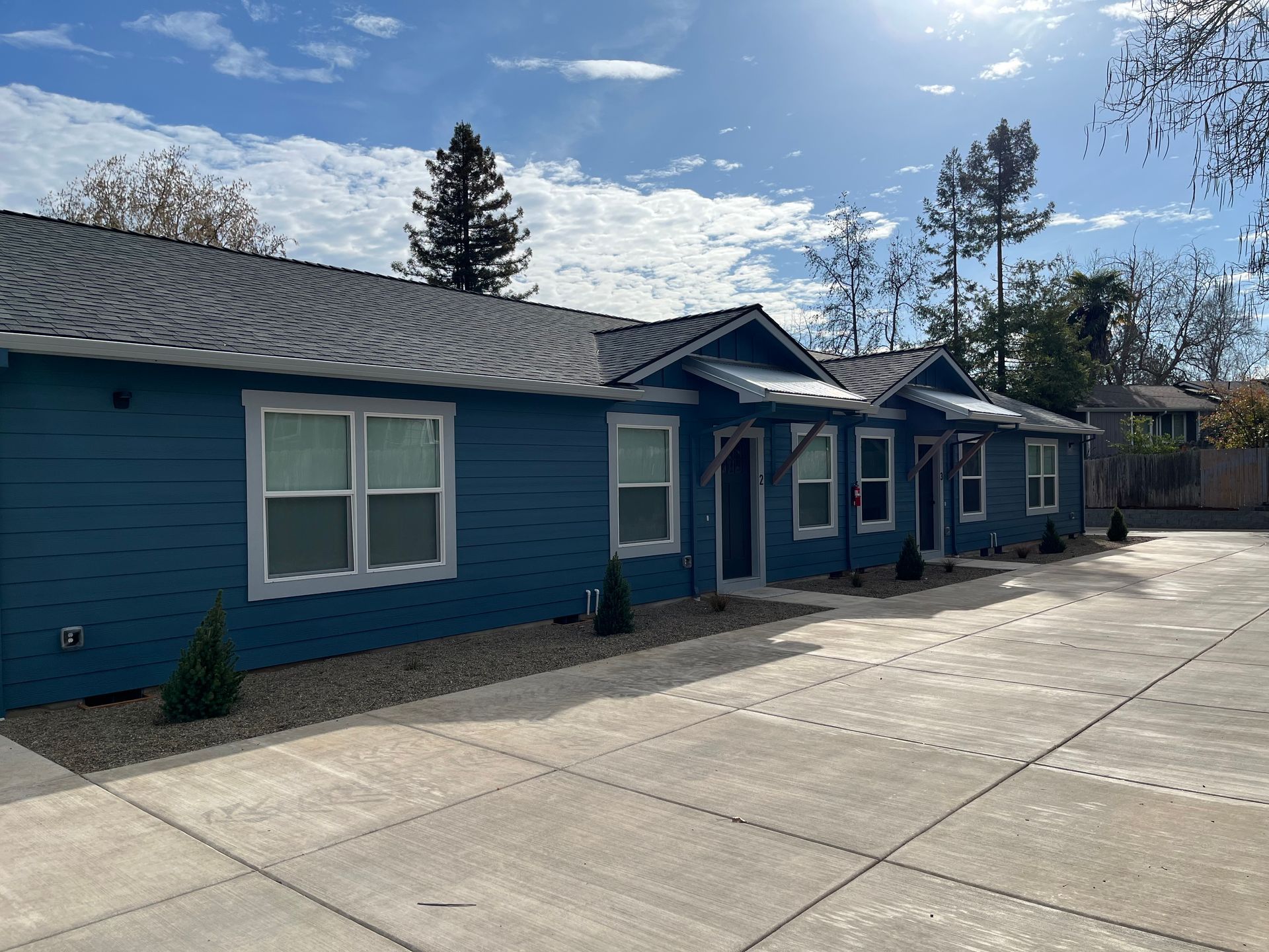 Blue single-story building with white-trimmed windows and a paved driveway under a bright sky.