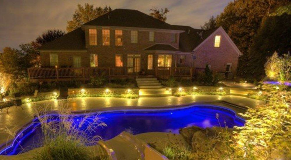 A large house with a swimming pool in front of it at night.