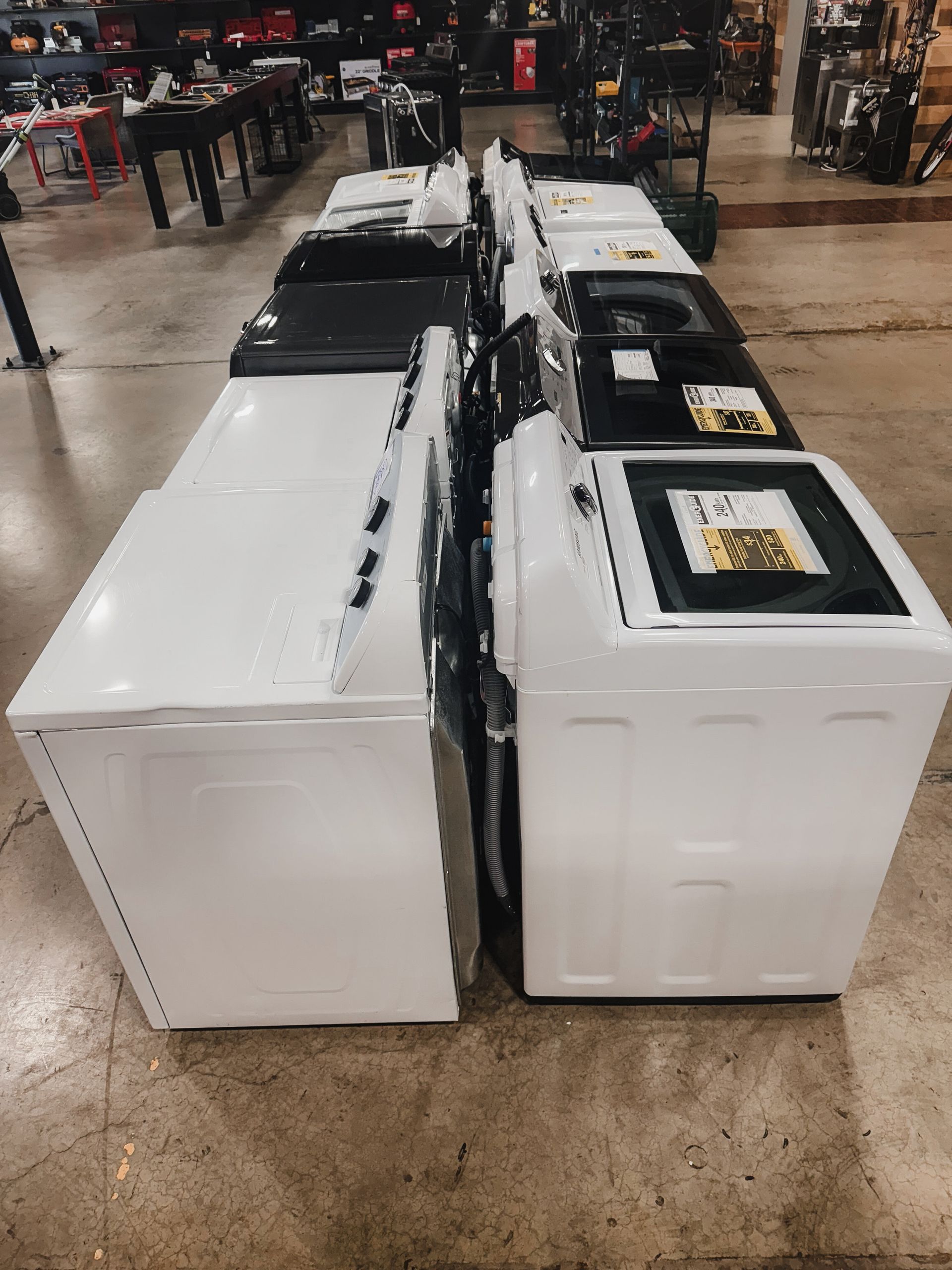 A row of white washers and dryers are lined up in a store.