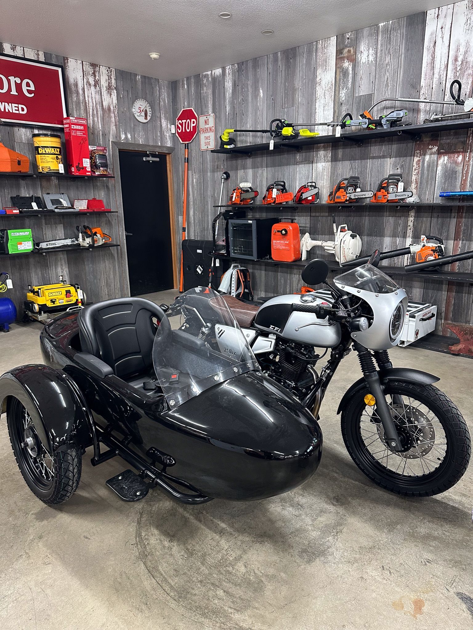 Motorcycle with black sidecar parked in a shop, shelves with tools in the background.