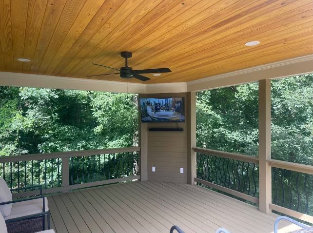 A screened in porch with a ceiling fan and a flat screen tv