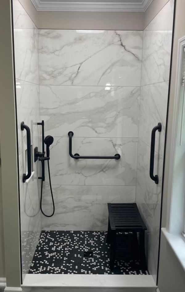 A bathroom with a walk in shower with black handles and a bench.