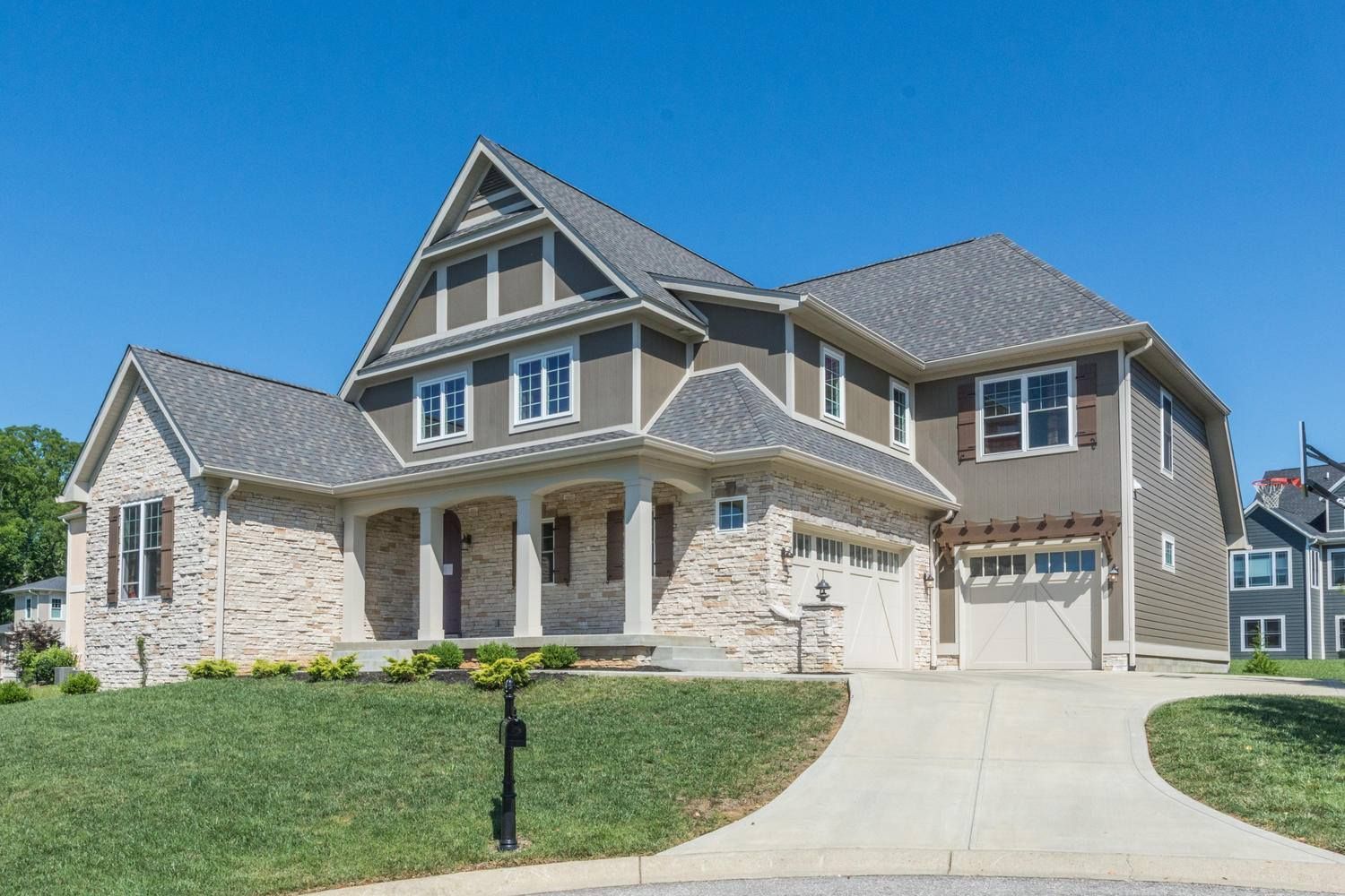 Two story house with stone facade, tan siding, and gray roof under a clear blue sky.