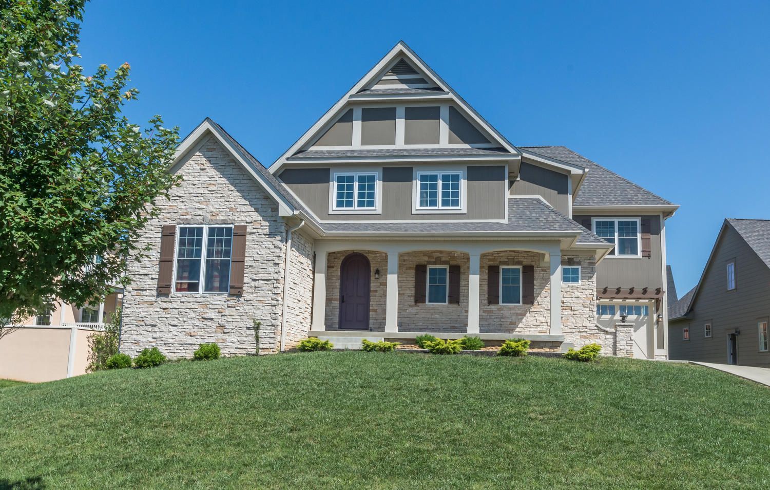 Two-story house with stone and gray siding, arched front door, and manicured lawn under a blue sky.